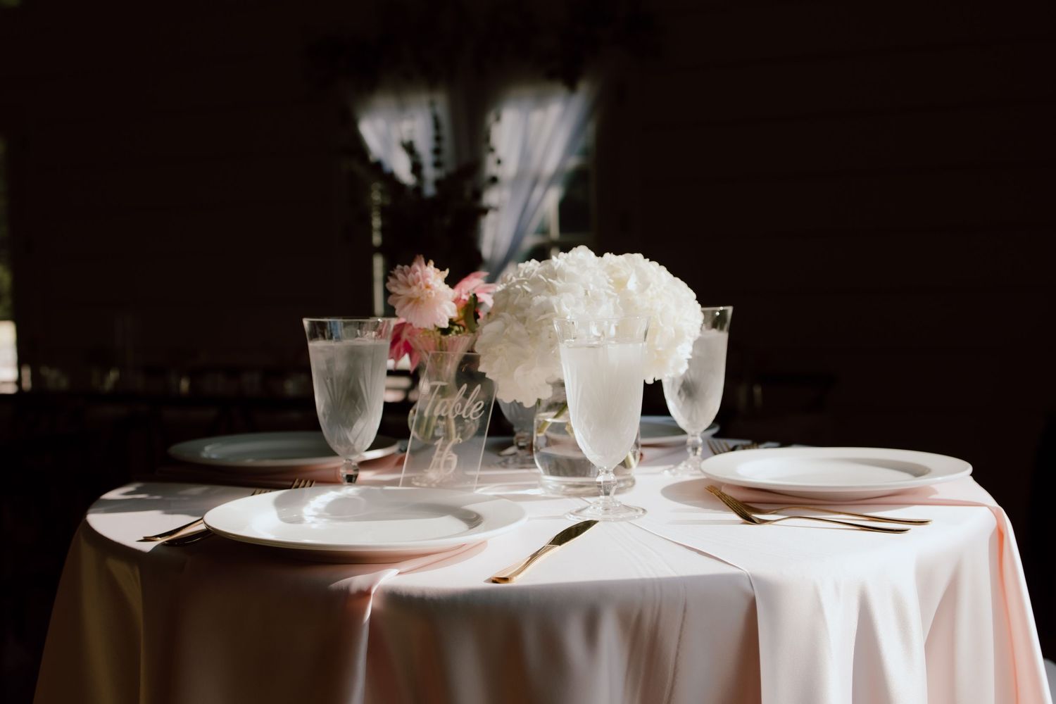 Wedding reception table setup with elegant table numbers, pink tablecloths, and direct sunlight for documentary style photography in NWA.