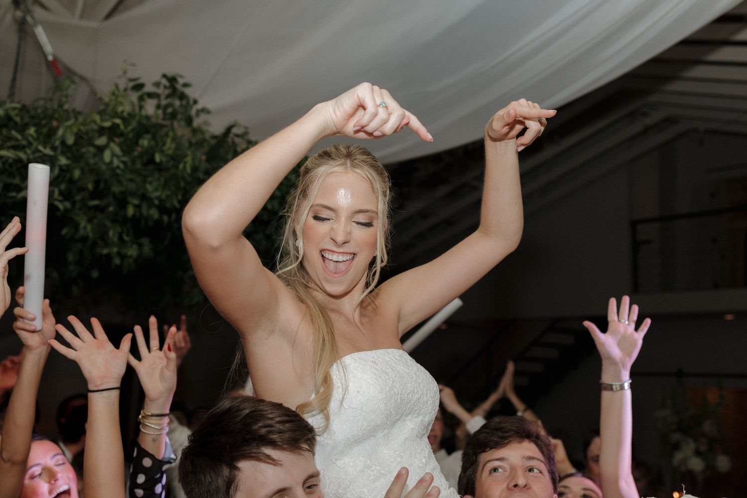 Bride on the dance floor celebrating as she is lifted in the air by guests.