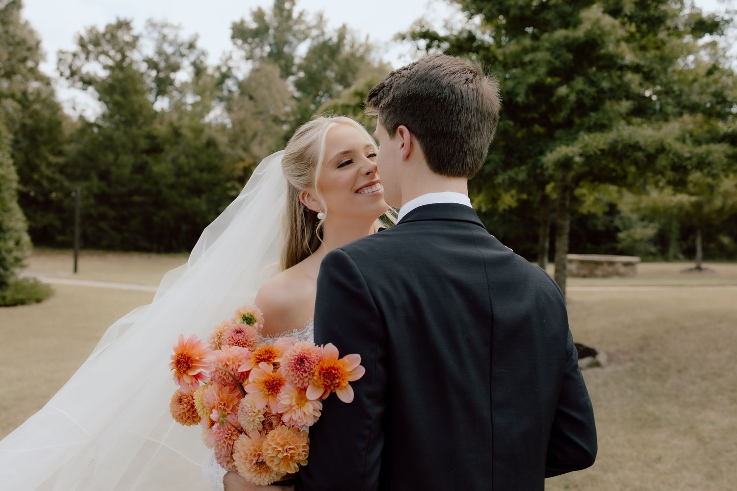 Candid, true to life Arkansas wedding photography of couple laughing on their wedding day with peach summer bridal bouquet.