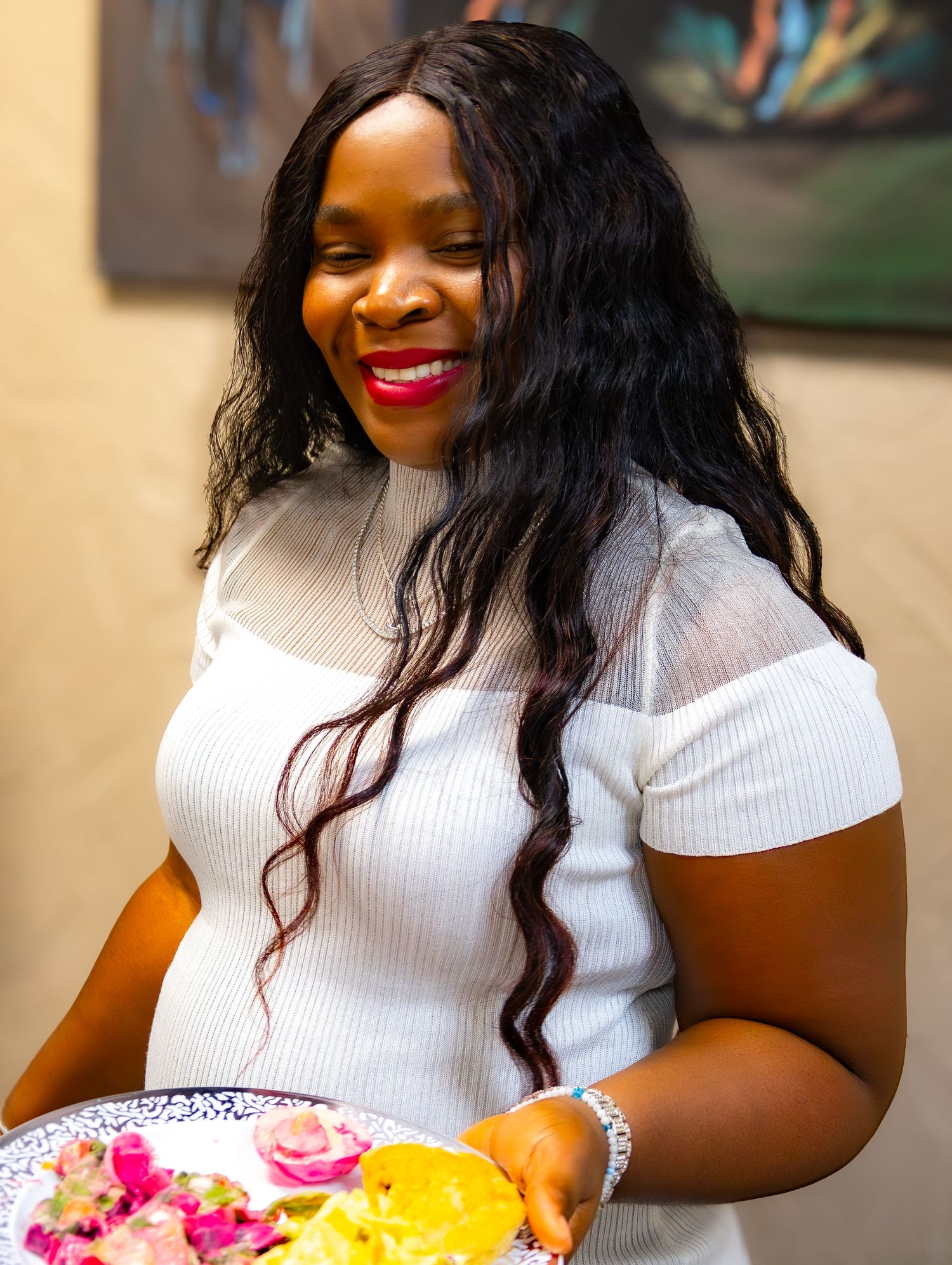 Smiling woman in white off-shoulder top holding colorful floral plate at indoor event.