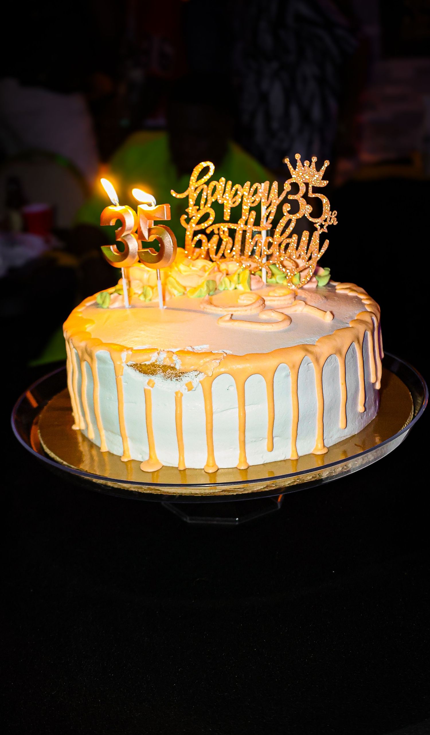 Elegant white and gold drip birthday cake with lit candles and a Happy 35th Birthday topper on a dark background.