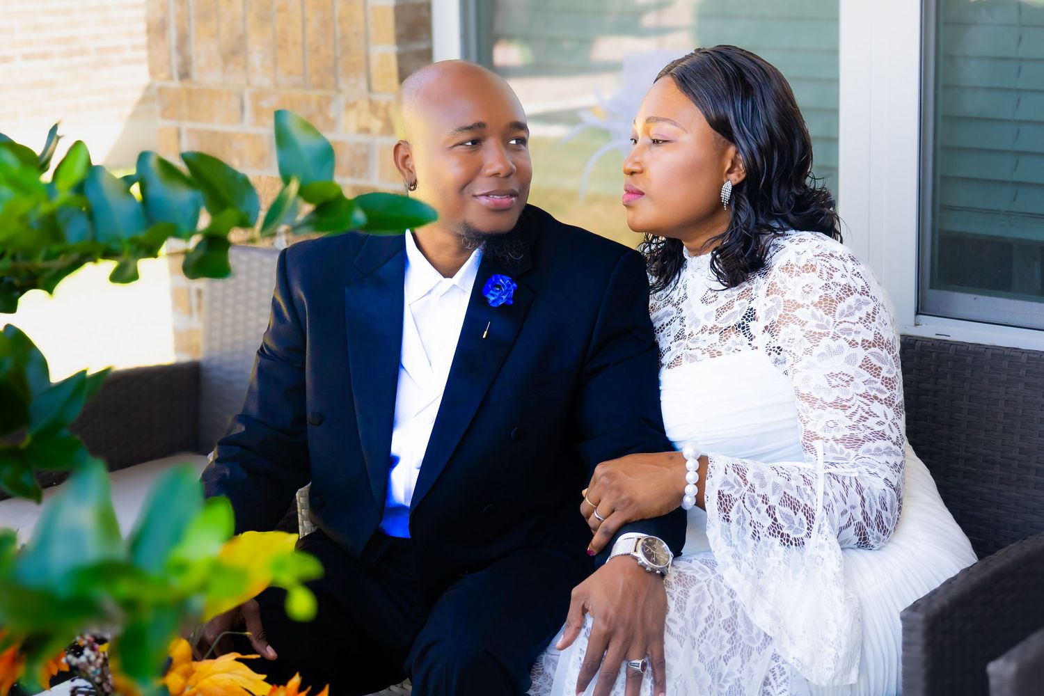 Elegant couple in formal attire sitting together outdoors, groom in navy suit with blue boutonniere.