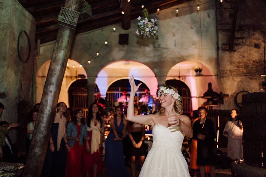 Wedding guests dance and celebrate under twinkling lights in a rustic stone venue during an evening reception.