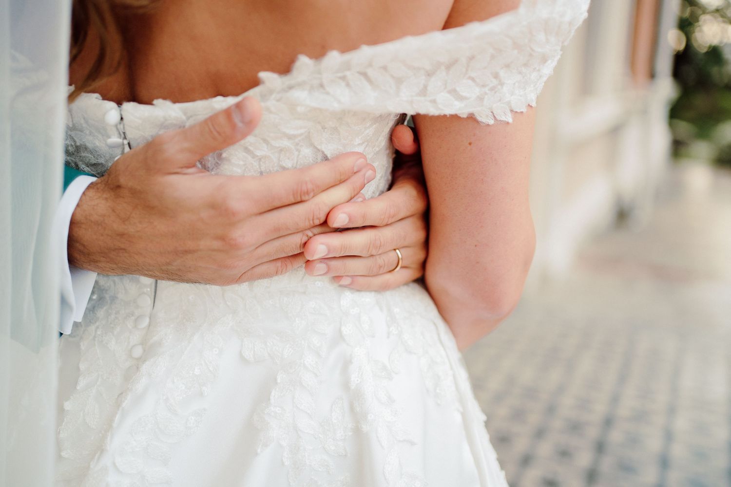 dettaglio fotografico alle mani dello sposo mentre abbraccia sua moglie in abito bianco.
