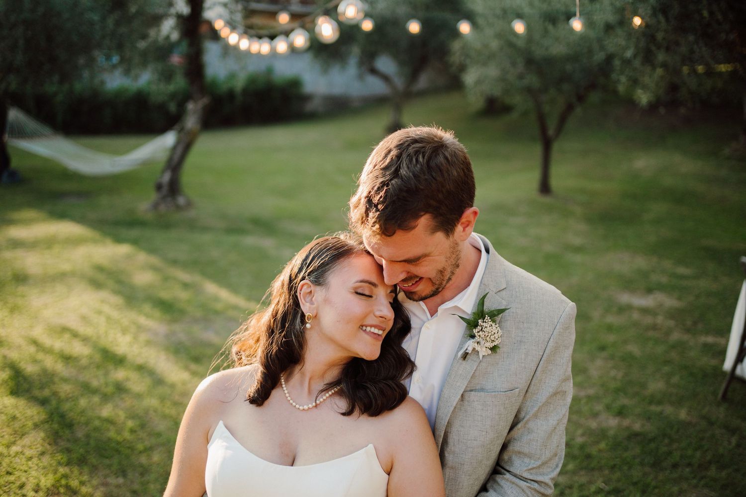Garden wedding portrait with string lights creating romantic ambiance at sunset.