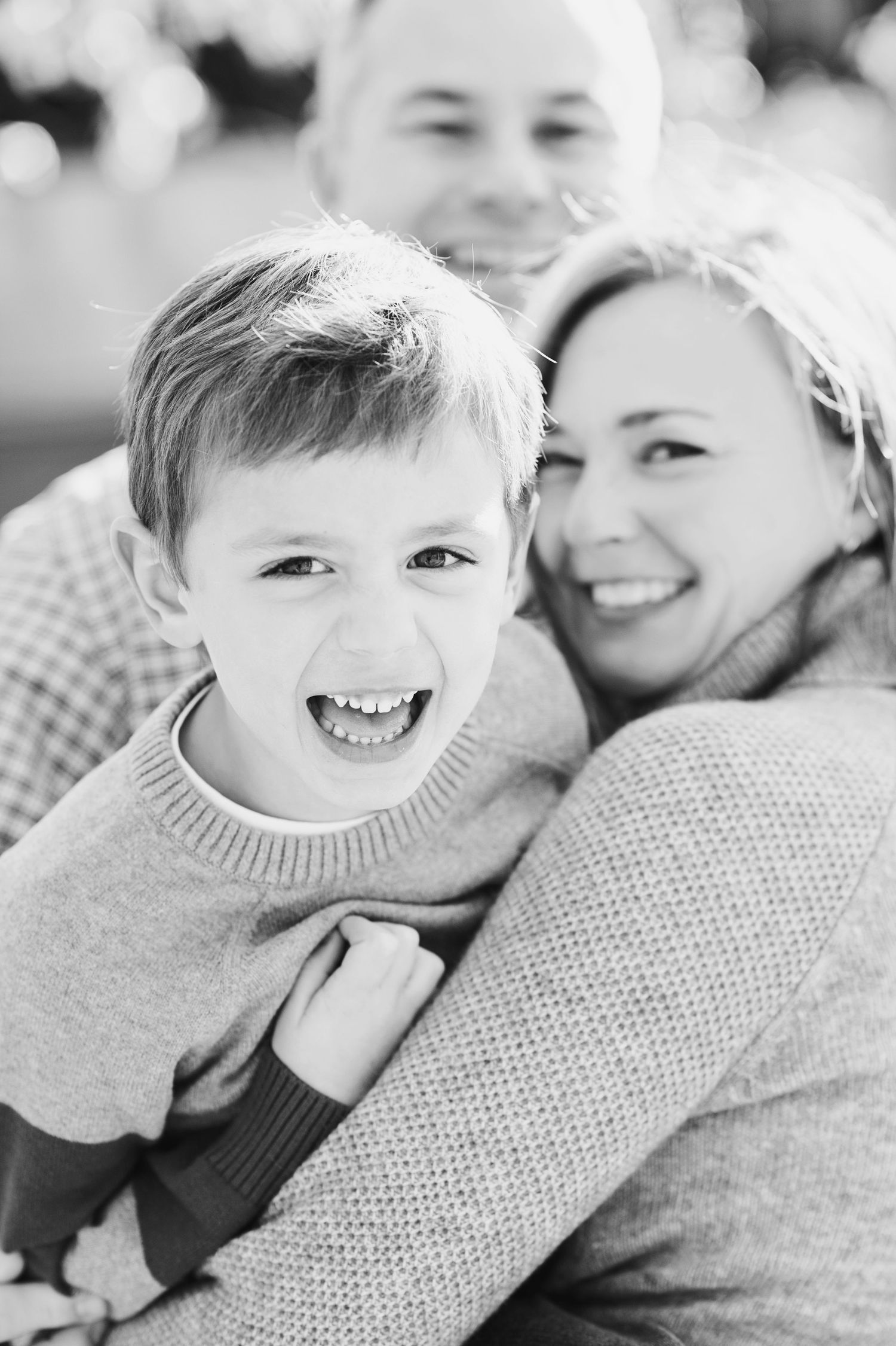 Black and white portrait of a joyful family sharing a warm embrace and laughing together outdoors.