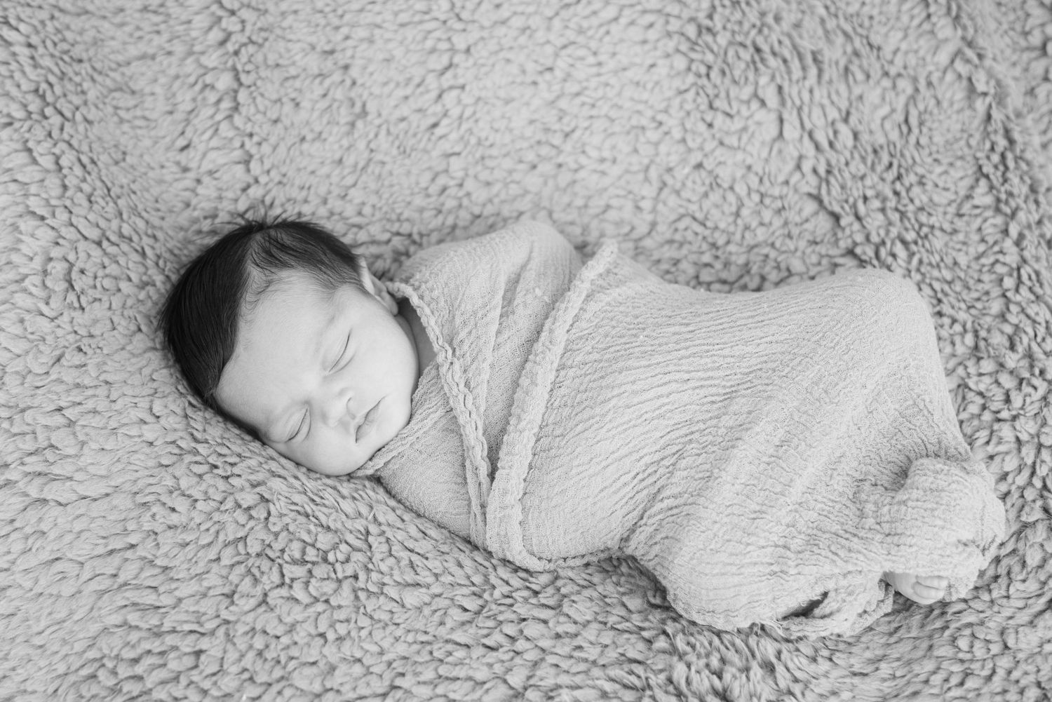 A sleeping newborn baby in a white onesie rests peacefully on a soft textured blanket.