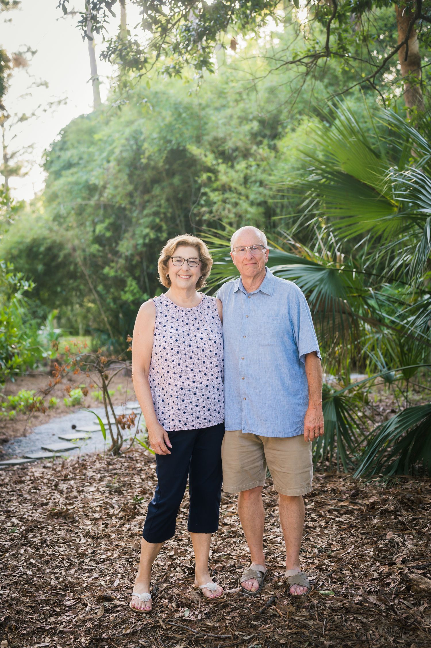 Couple poses on mulched path surrounded by tropical plants and palm trees.Hammock Beach, Sea Pines coastal photography.