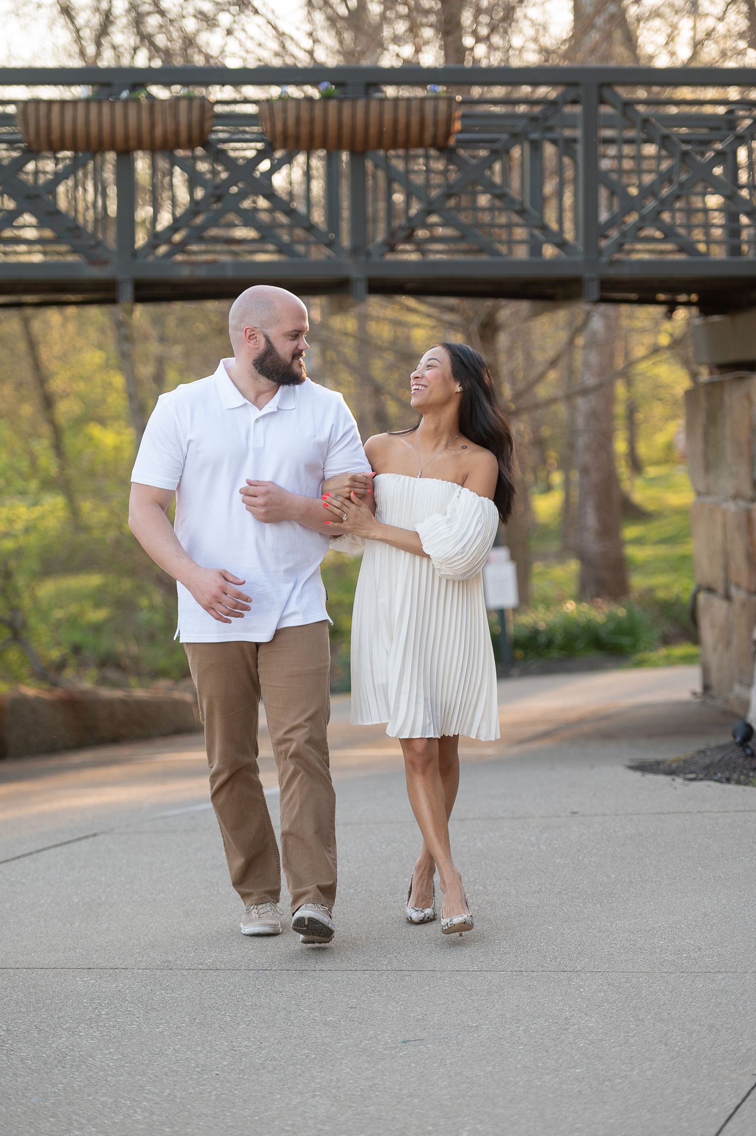 A couple in white and khaki outfits dance together on a paved path beneath a bridge during sunset. Ohio engagement session.