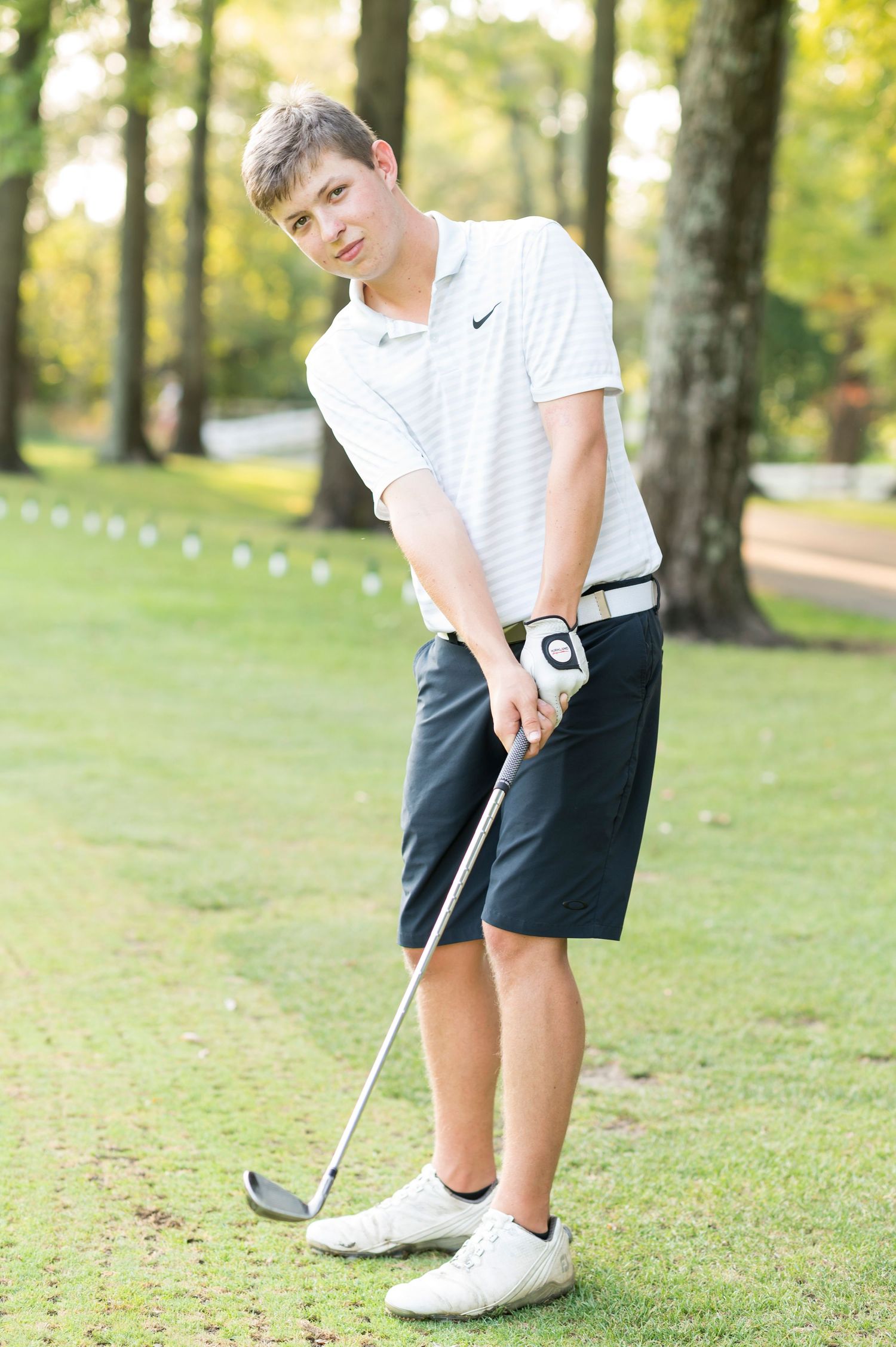 Young golfer in white shirt and black shorts practices putting technique on grassy course.