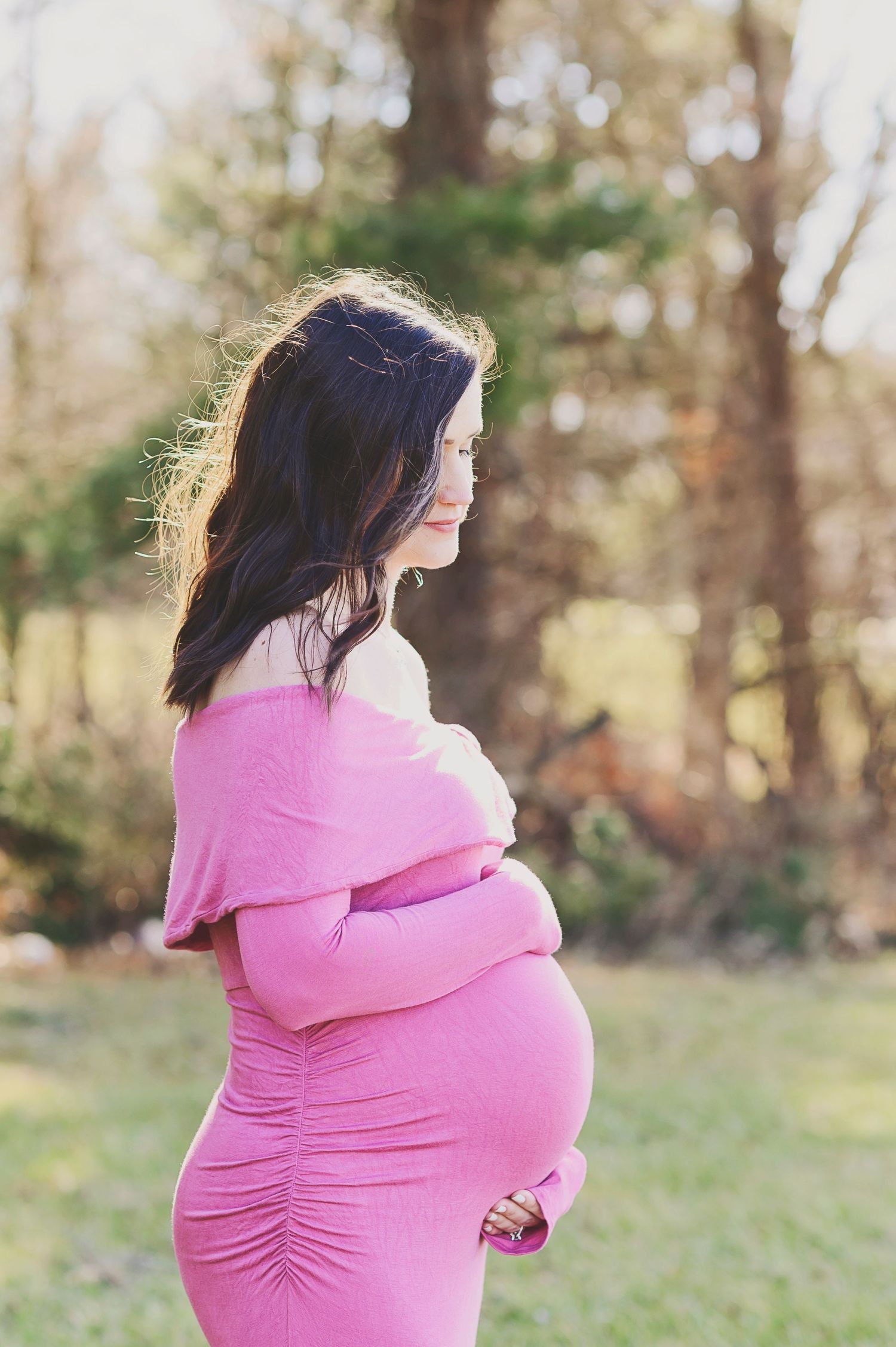 Side view of expectant mother in pink dress showing baby bump during outdoor maternity shoot.
