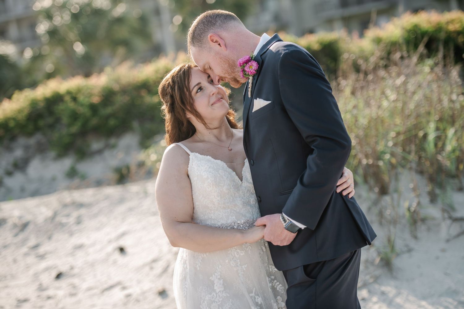 A romantic beach wedding photoshoot with couple embracing against a sandy dune backdrop at sunset. Hilton Head