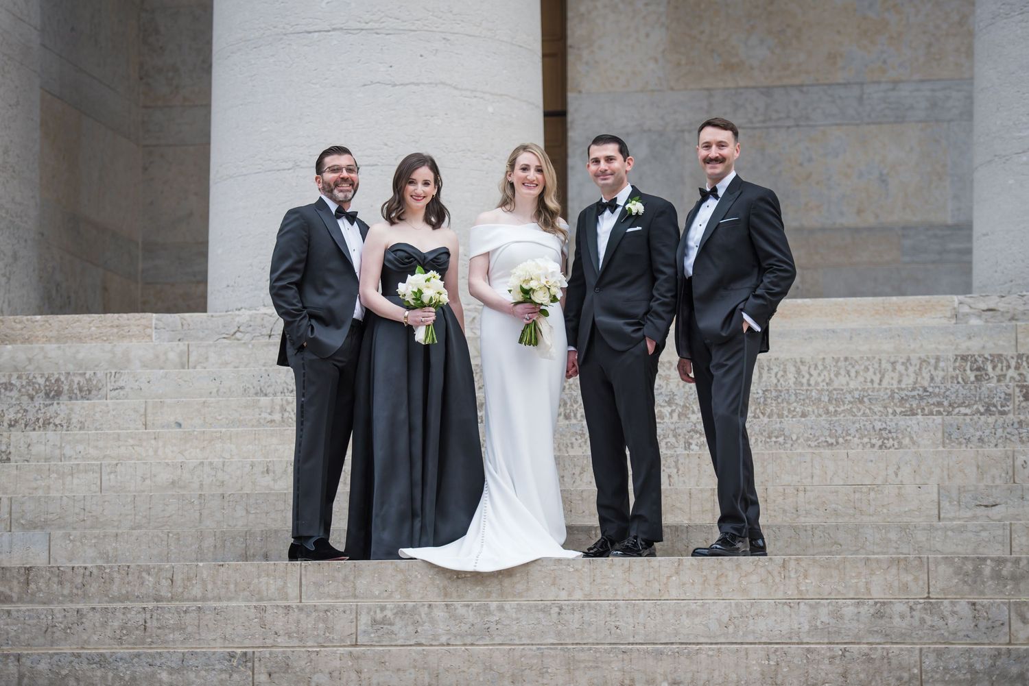 Wedding party poses on stone steps in formal attire.