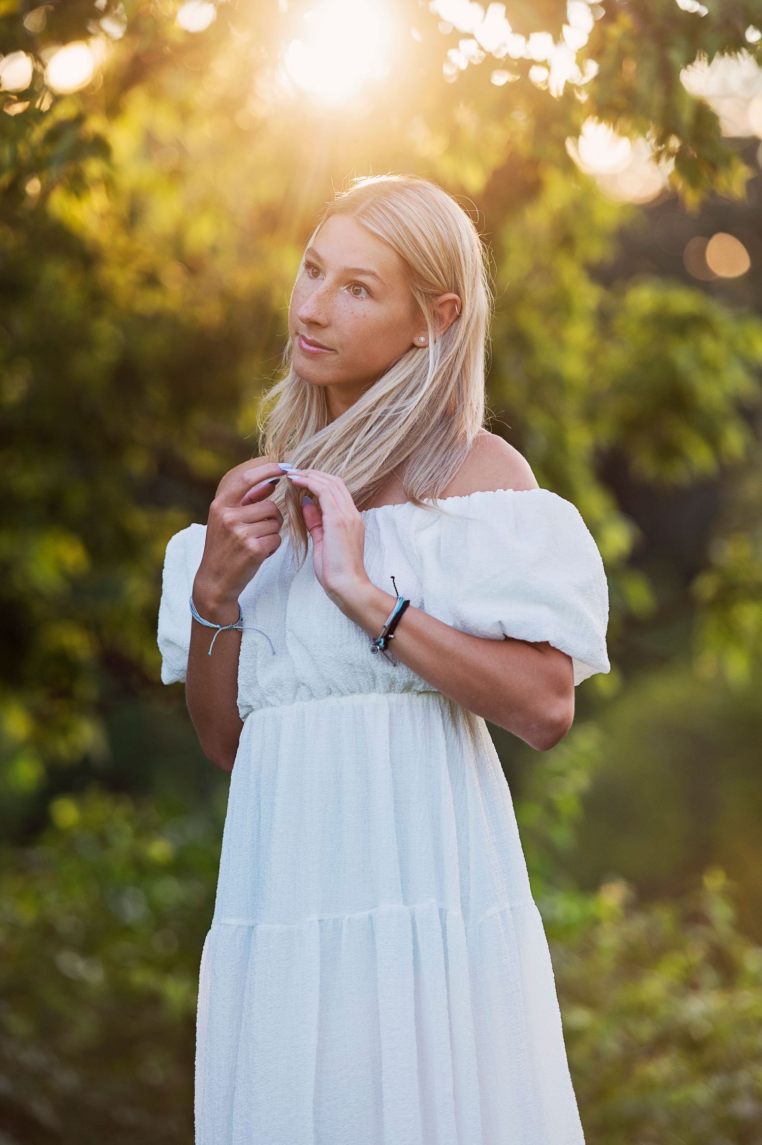 A white off-shoulder dress captured in golden sunset light with bokeh effect through trees.