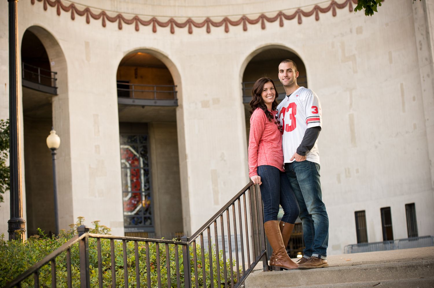 A couple stands together in an outdoor courtyard with arched architectural details and string lights overhead. Ohio Stadium