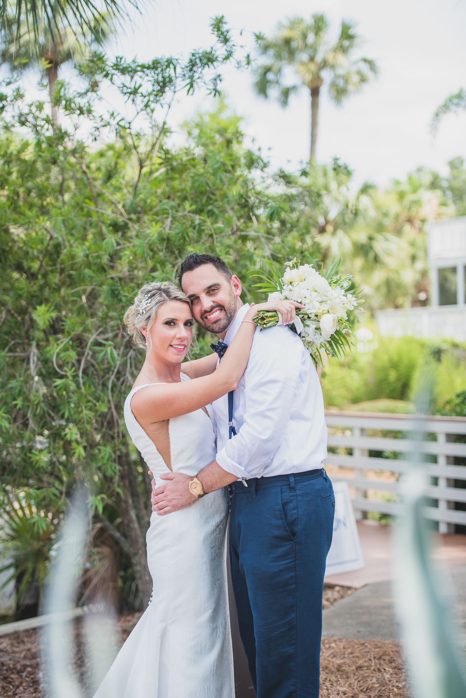 Hilton Head Wedding couple embraces in front of lush greenery and palm trees during outdoor photo session.