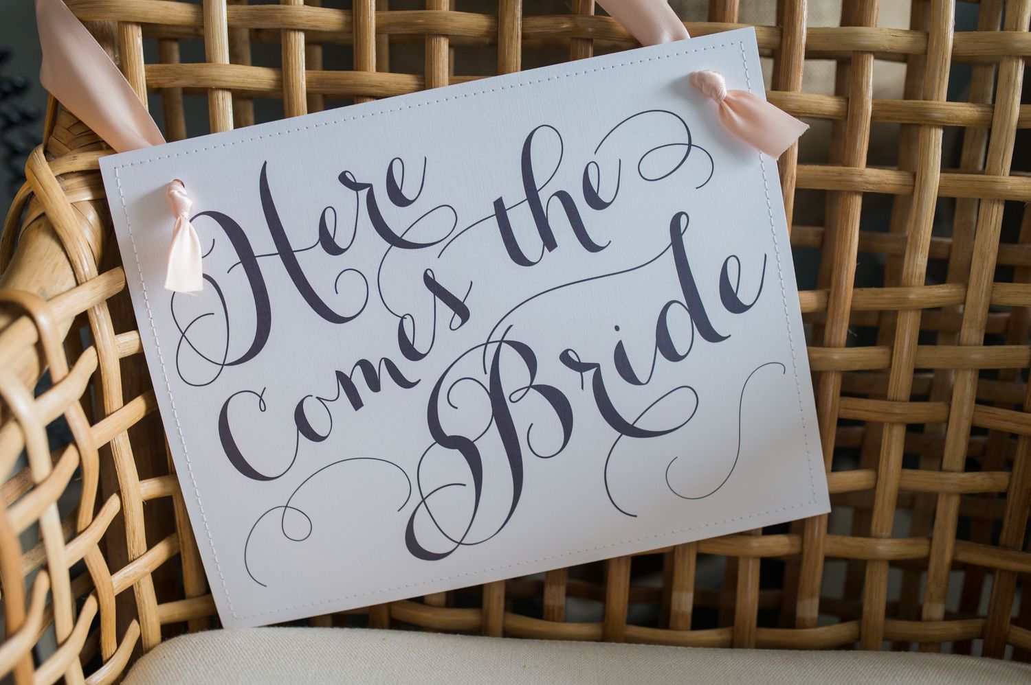 Elegant calligraphy wedding signs with decorative flourishes on woven bamboo background.