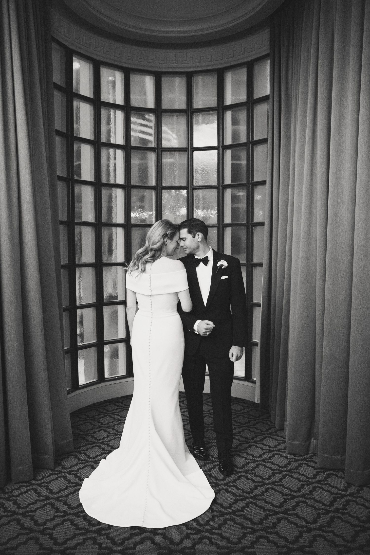 Elegant black and white wedding portraits in a grand room with arched windows and patterned carpet.