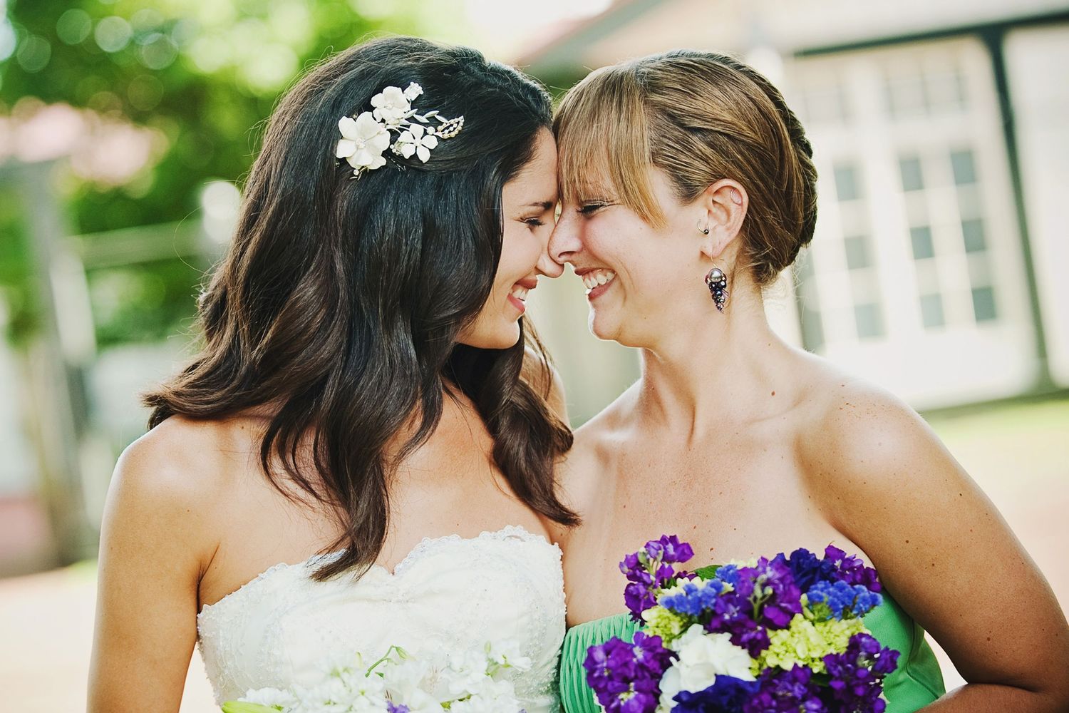 Two people in wedding attire share a joyful moment together with one holding a vibrant purple and yellow bouquet.