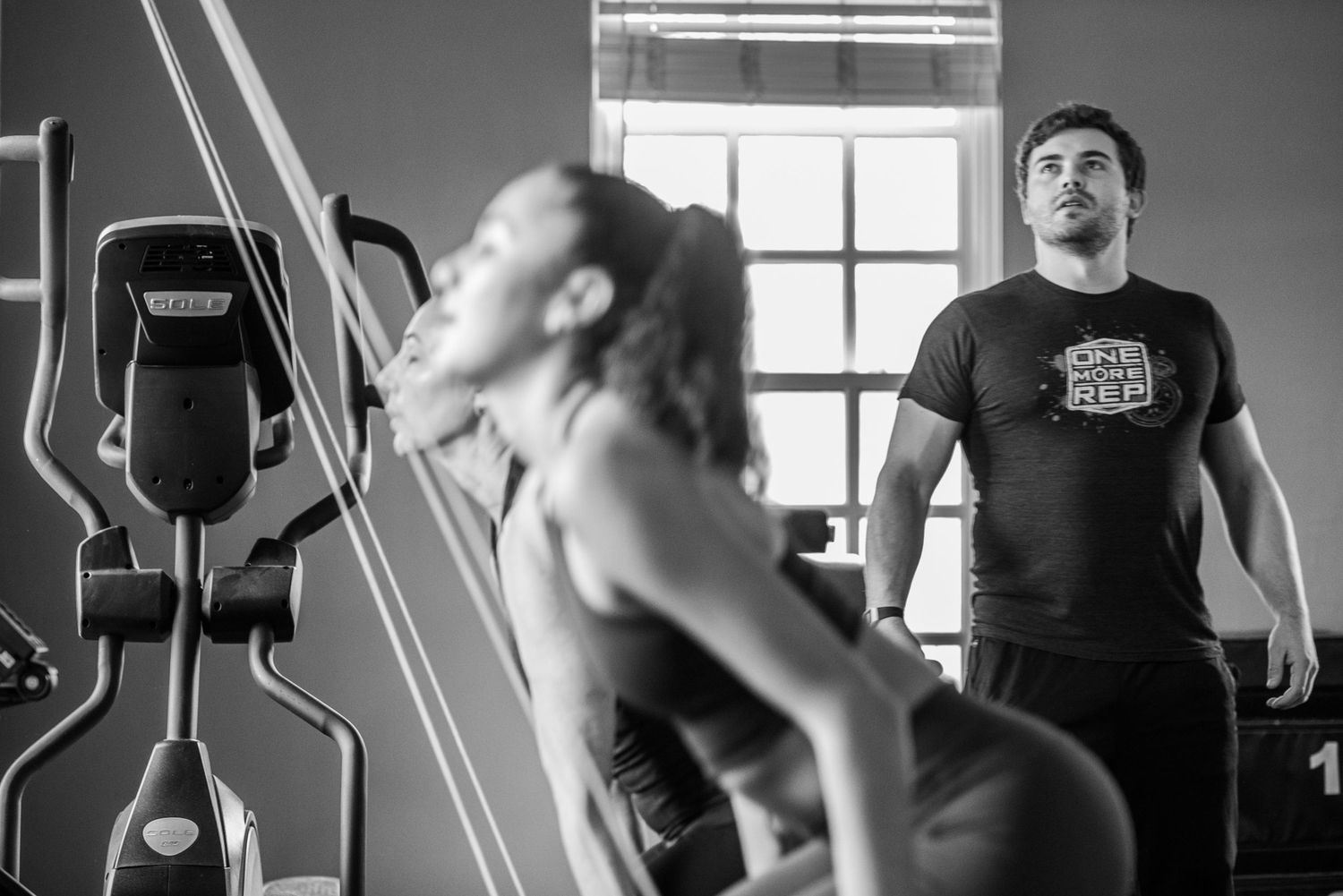 People working out with fitness equipment in a black and white gym setting.