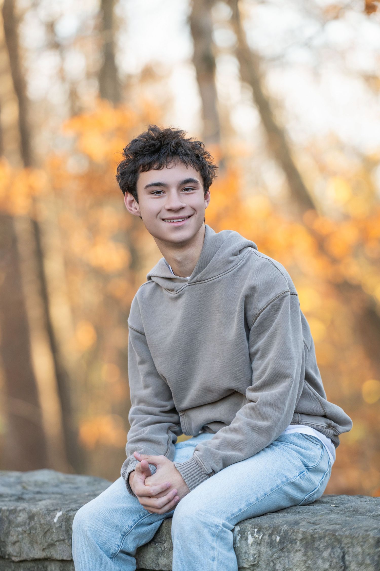 A series of four outdoor portraits showing someone in a gray sweatshirt sitting on a stone wall with autumn foliage in background.