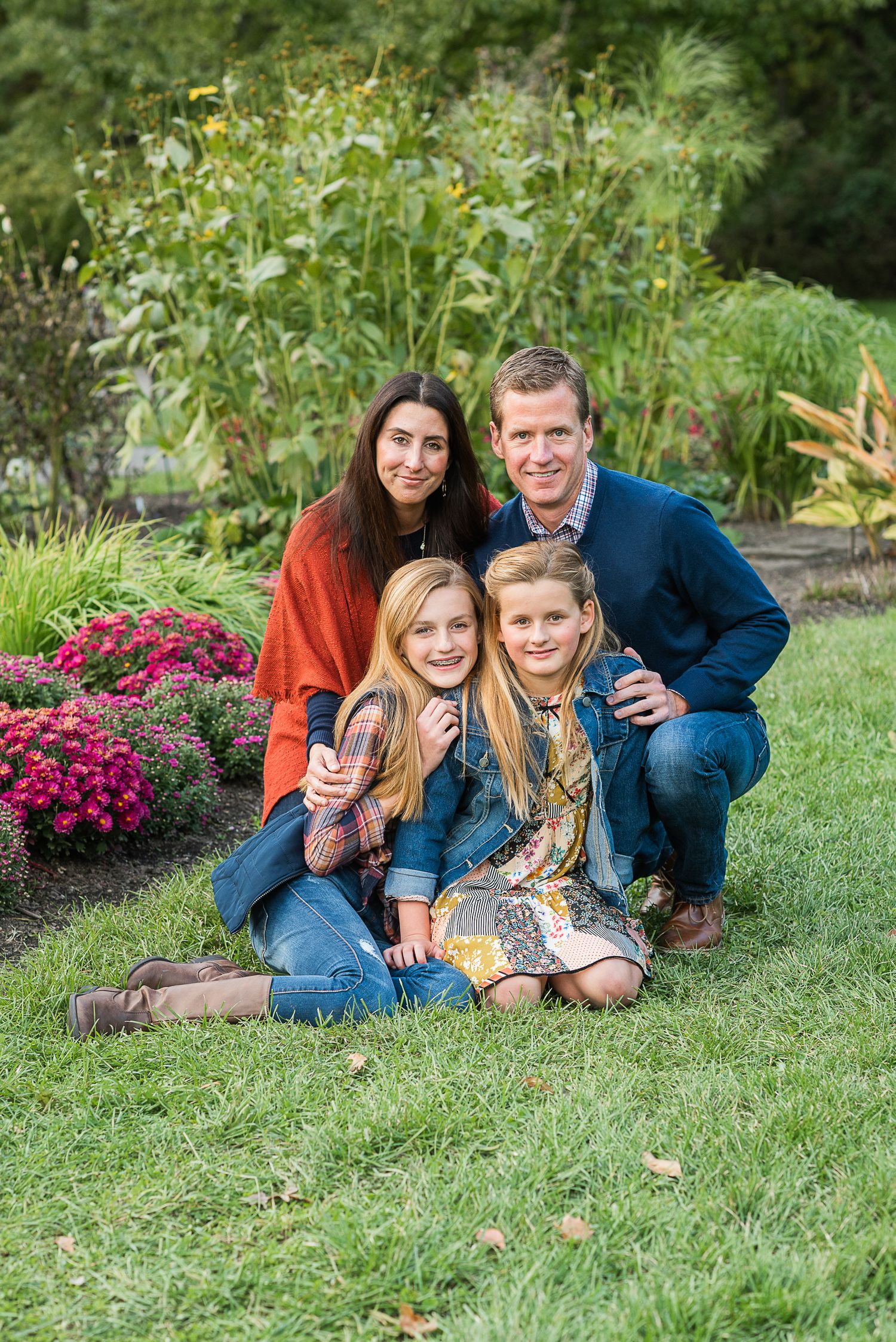 Family relaxing together on green grass with pink flowers blooming in garden background.