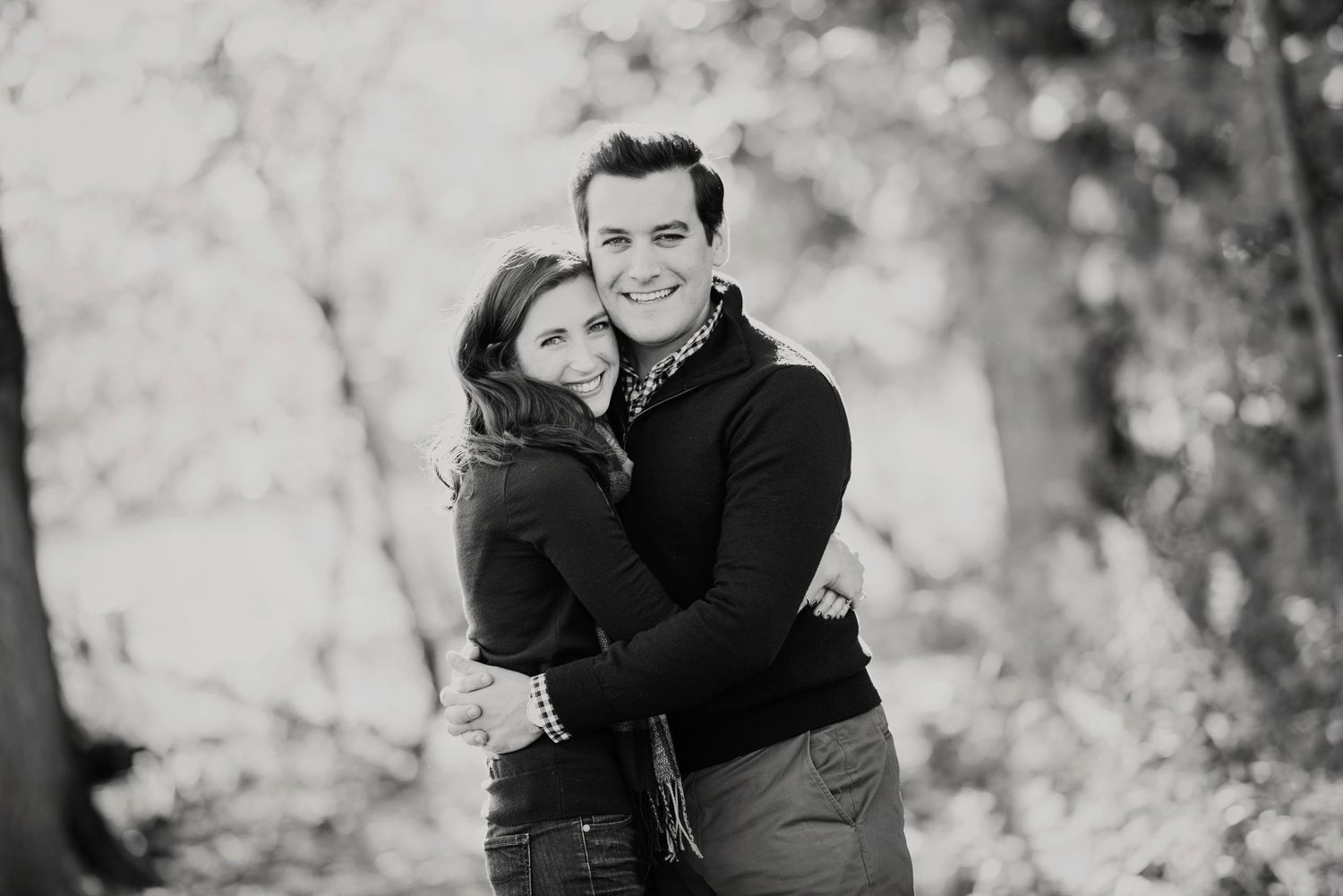 A romantic black and white portrait of a couple embracing outdoors with soft bokeh background.