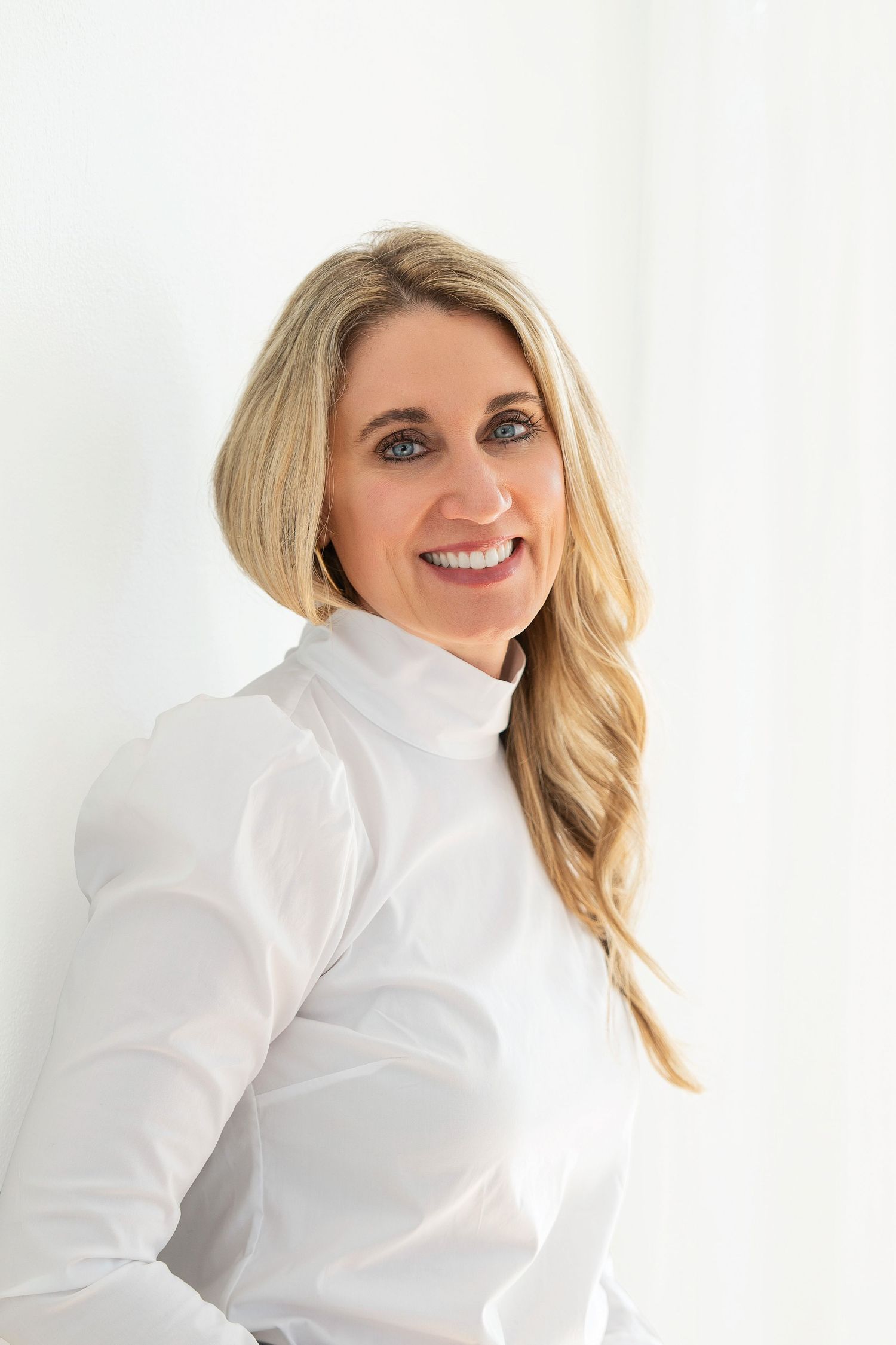 Professional studio headshot of someone in a crisp white button-down shirt against a light background, with a bright smile.