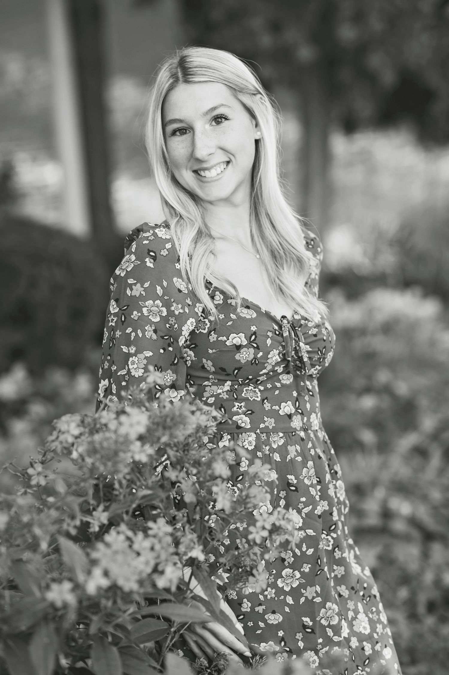 Black and white portrait in a garden setting with a floral print dress among blooming flowers.