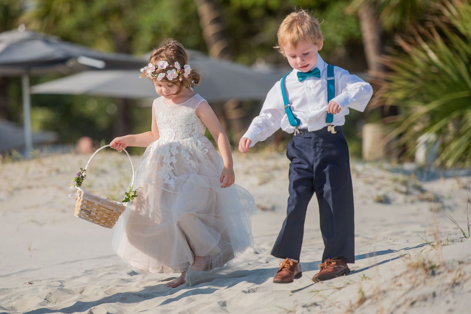 Wedding couple walking playfully on sandy beach near palm trees.