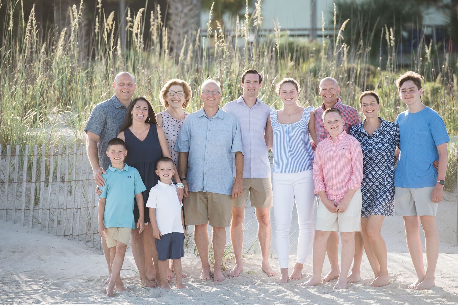 Group portrait of people gathered on a sandy beach with sea grass and dunes in the background.