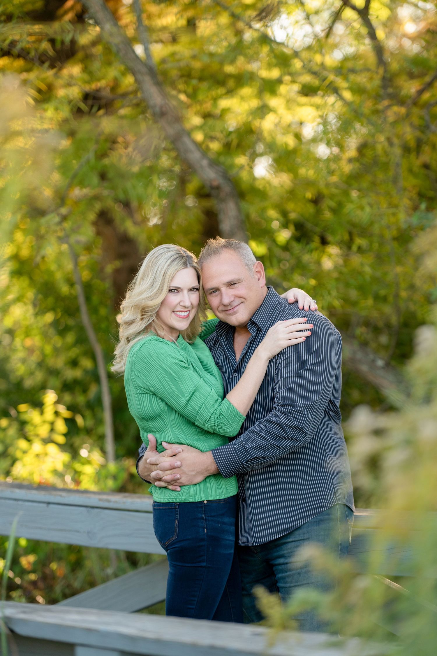 Couple embracing and laughing together outdoors with autumn foliage in the background.