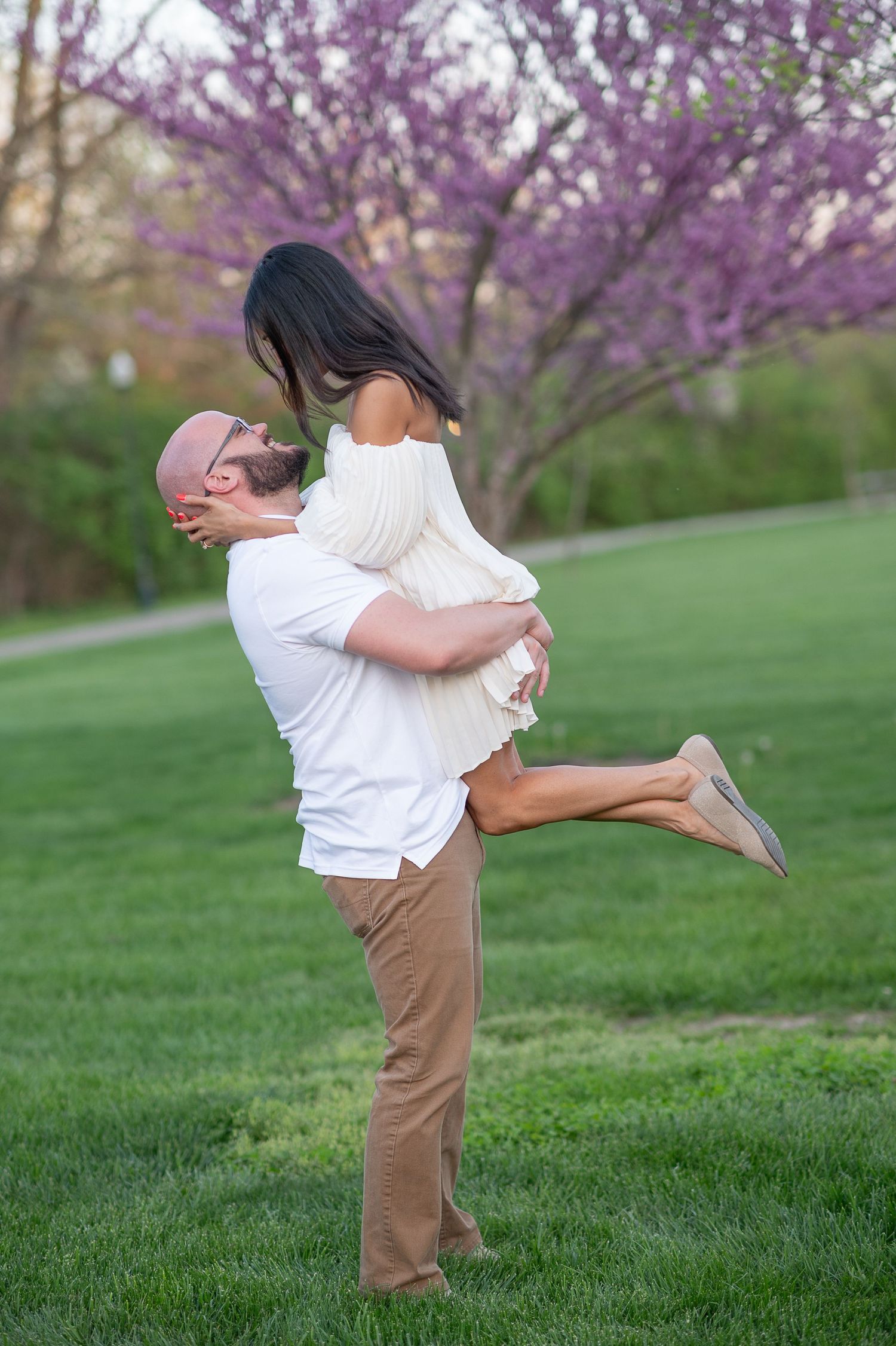 Ohio engagement session Playful couple spinning and embracing in field with purple flowering trees in background.