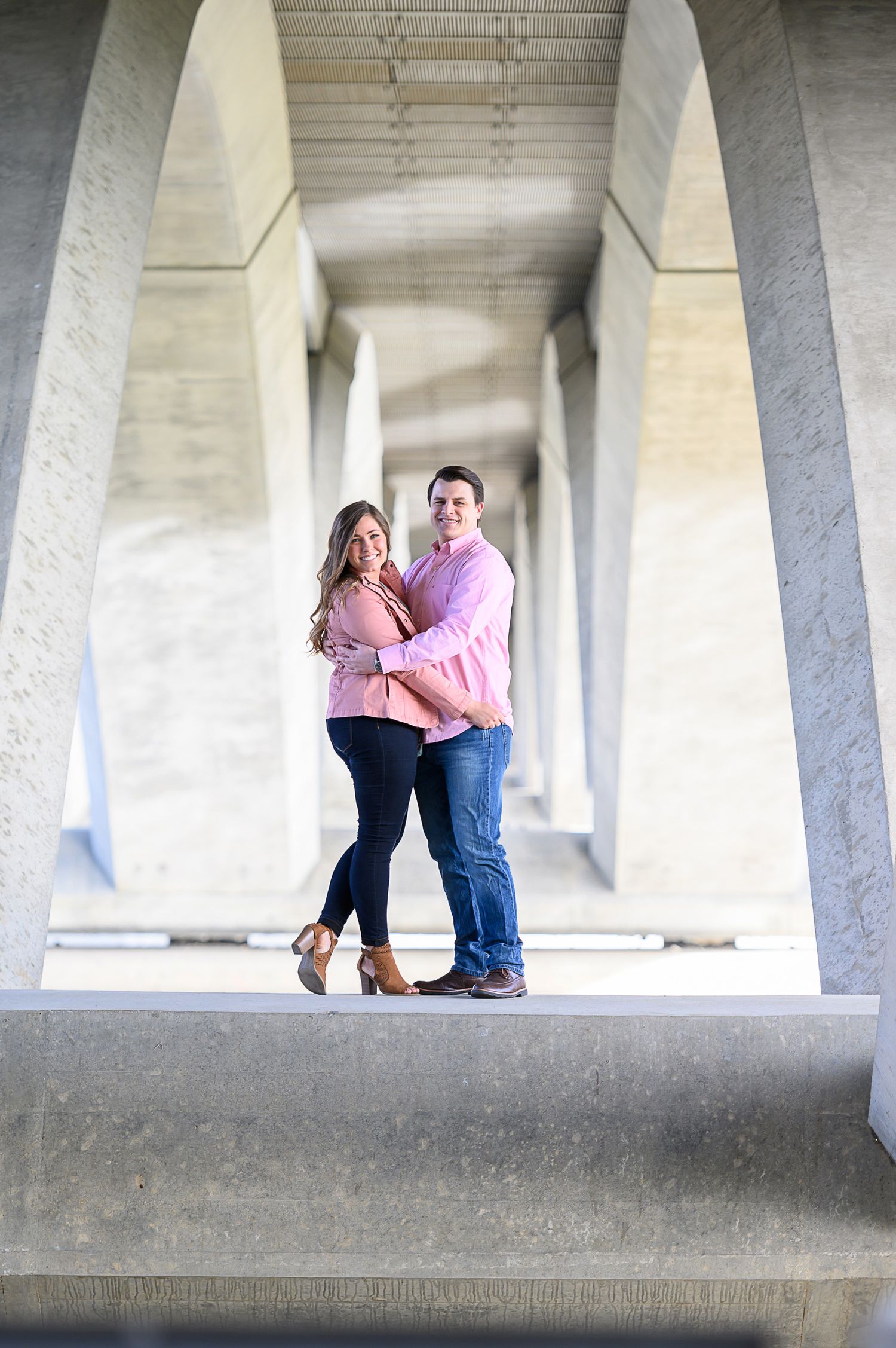 Couple in pink and denim sharing playful moments under concrete architecture.