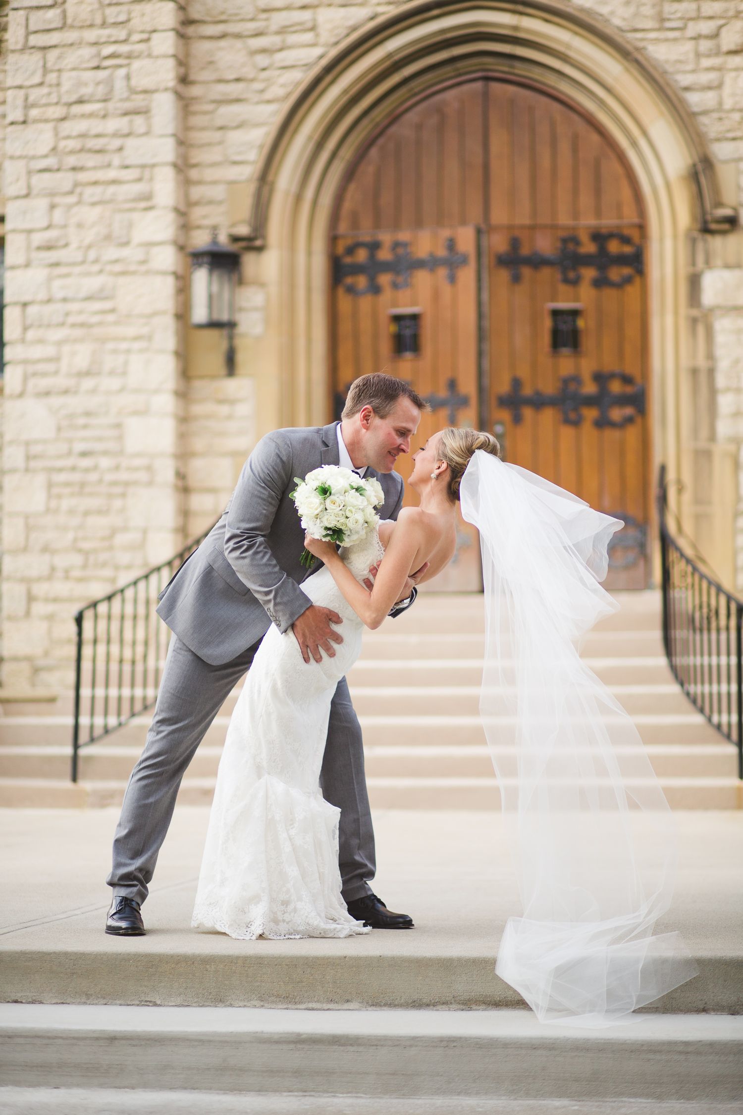 A romantic dip kiss sequence outside a stone church with arched wooden doors.