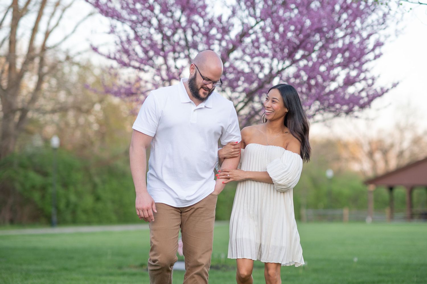 engagement session Couple poses together in a field with cherry blossom trees during golden hour.
