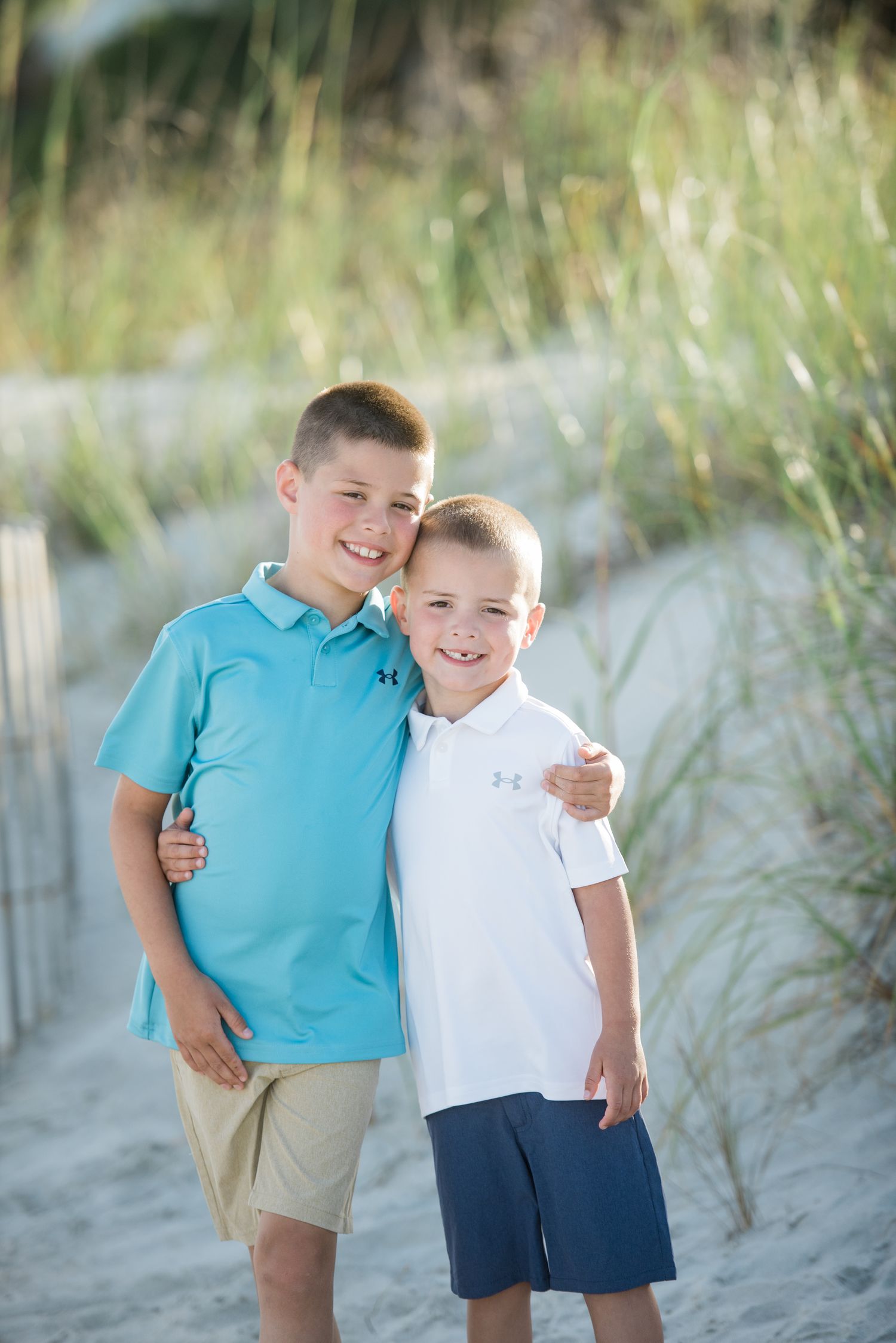 Siblings in coordinating blue and white outfits embrace while standing on beach sand. Palmetto Dunes