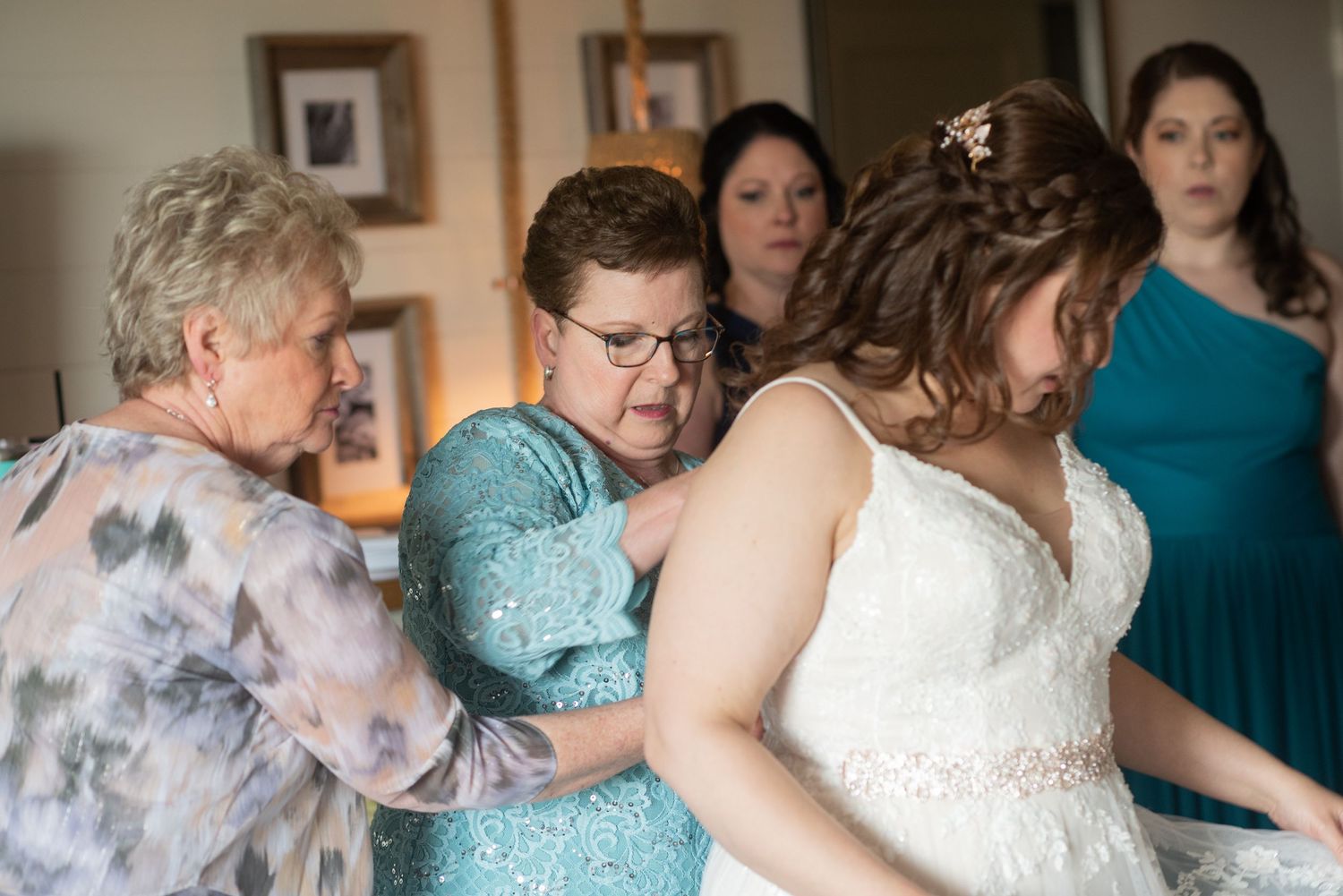 Wedding party in teal blue dresses helping with bridal preparations.
