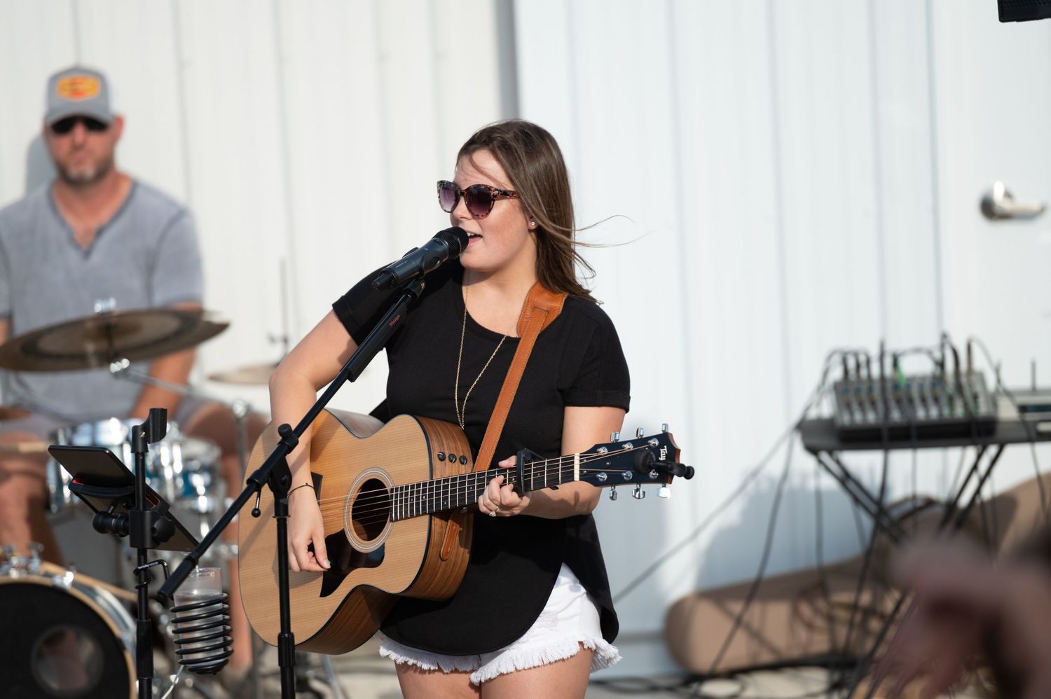 Musicians perform on acoustic guitars and drums at an outdoor venue during a live concert performance.