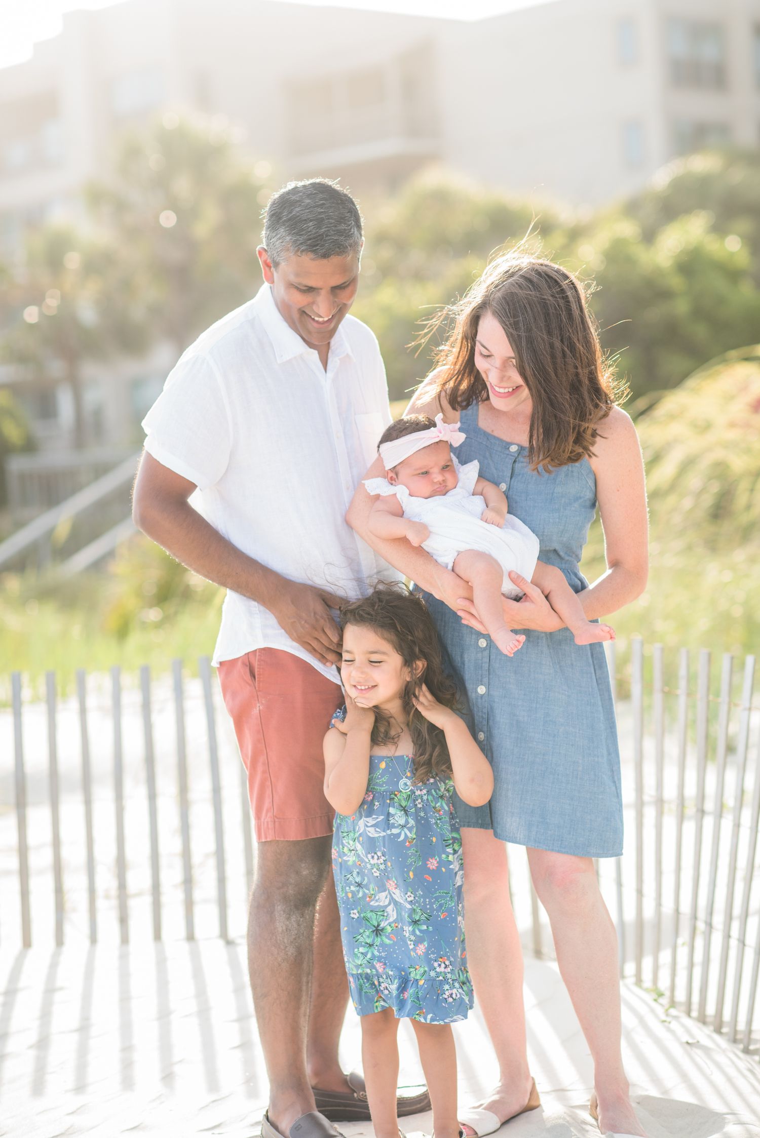 Family poses together on sandy beach with white fence in background. St. Augustine Beach, Hammock Beach photographer.