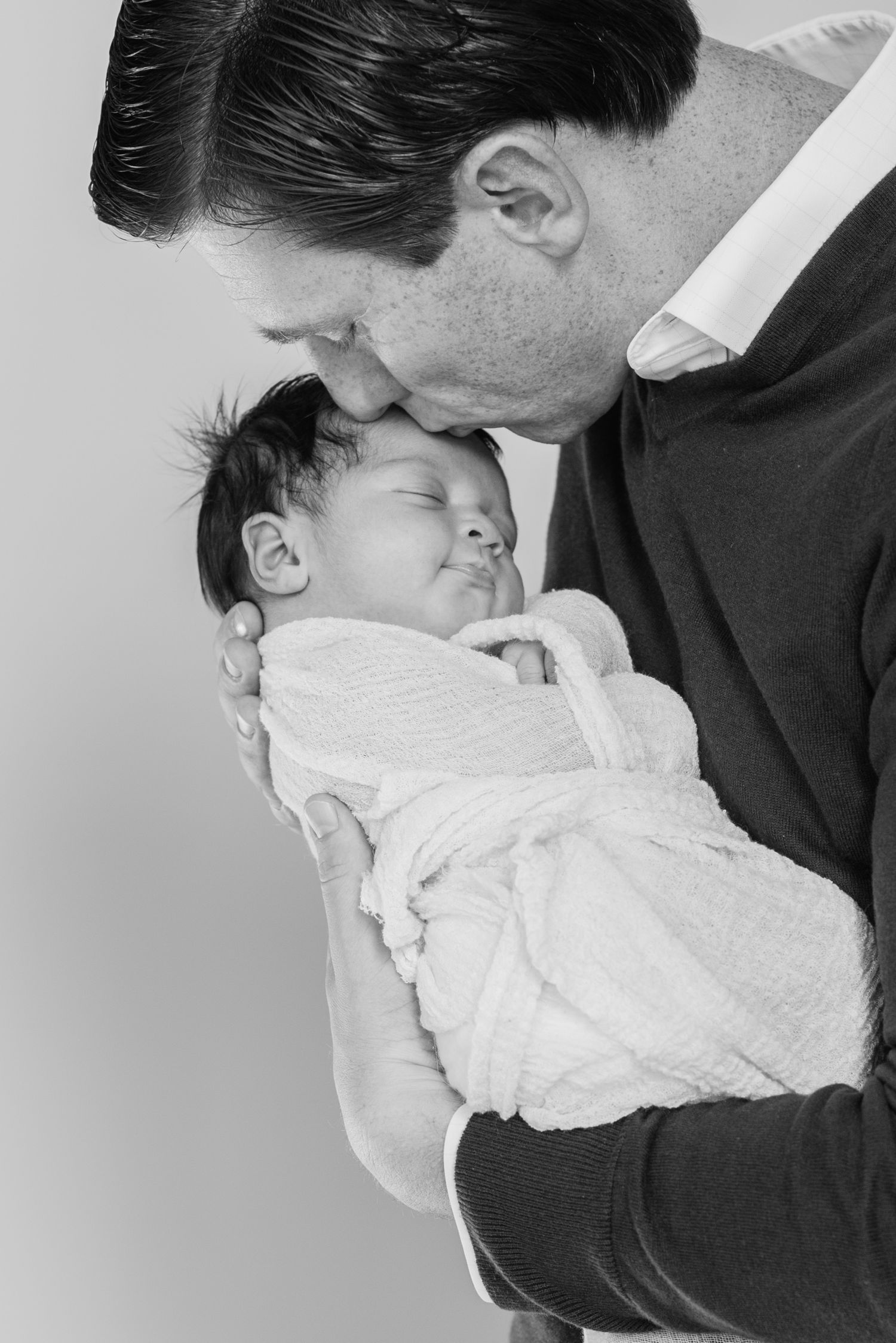 A series of tender moments between a couple kissing their newborn baby in white against a light background.