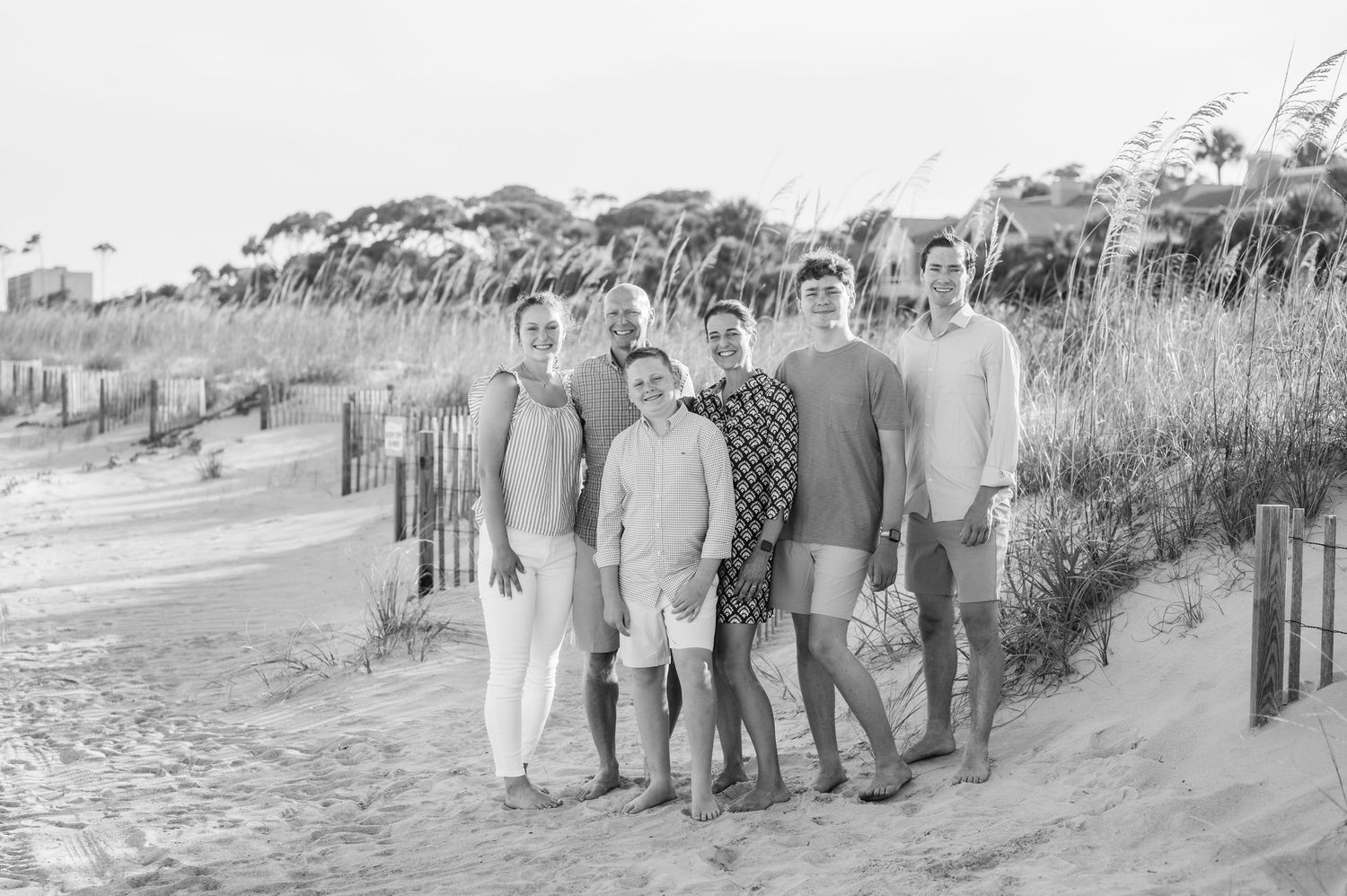Black and white beach portraits of family group with dunes and fencing in background.