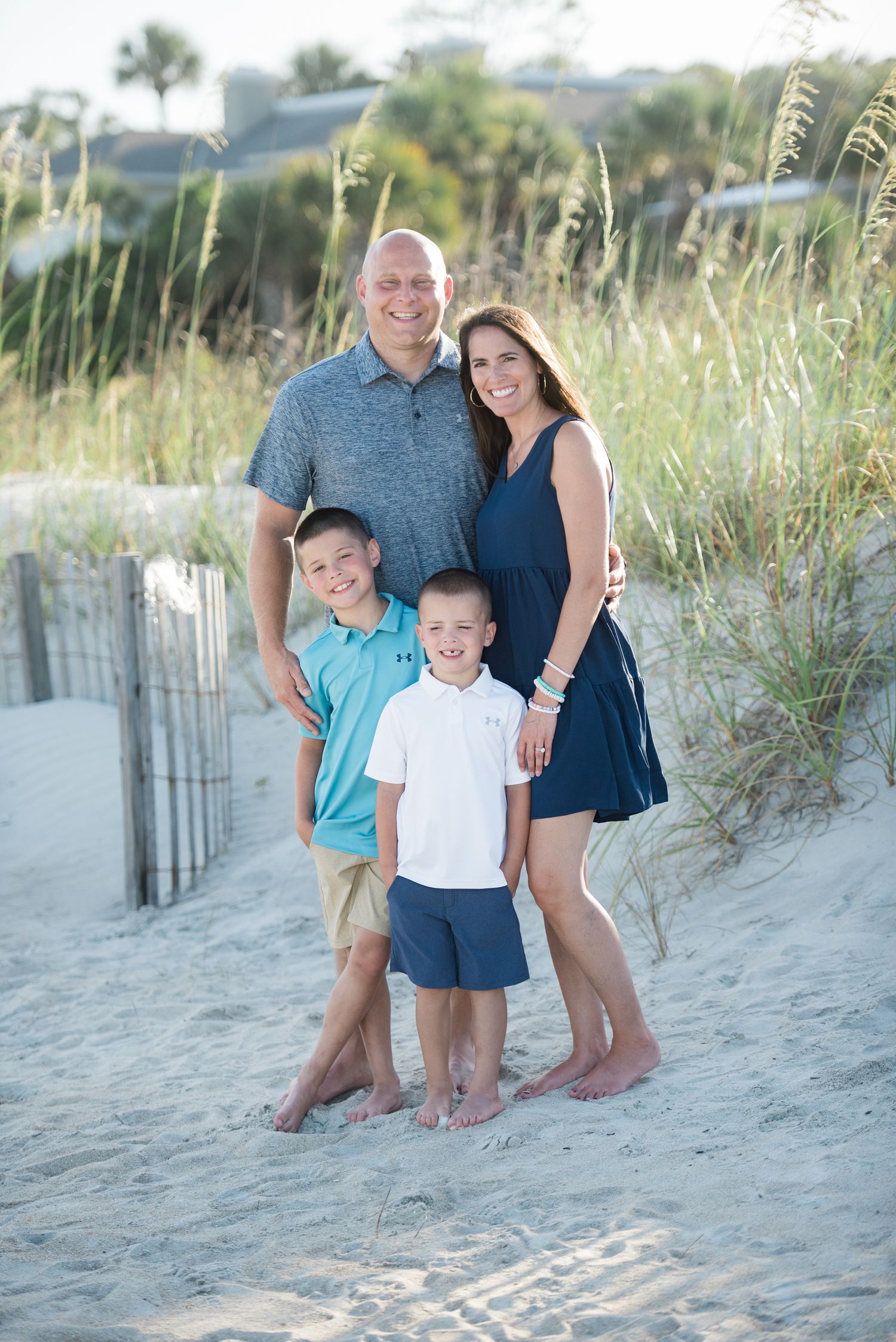 Candid family photos captured on a sandy beach with coastal vegetation and wooden fencing. Hammock Beach, Sea Pines coastal photography.