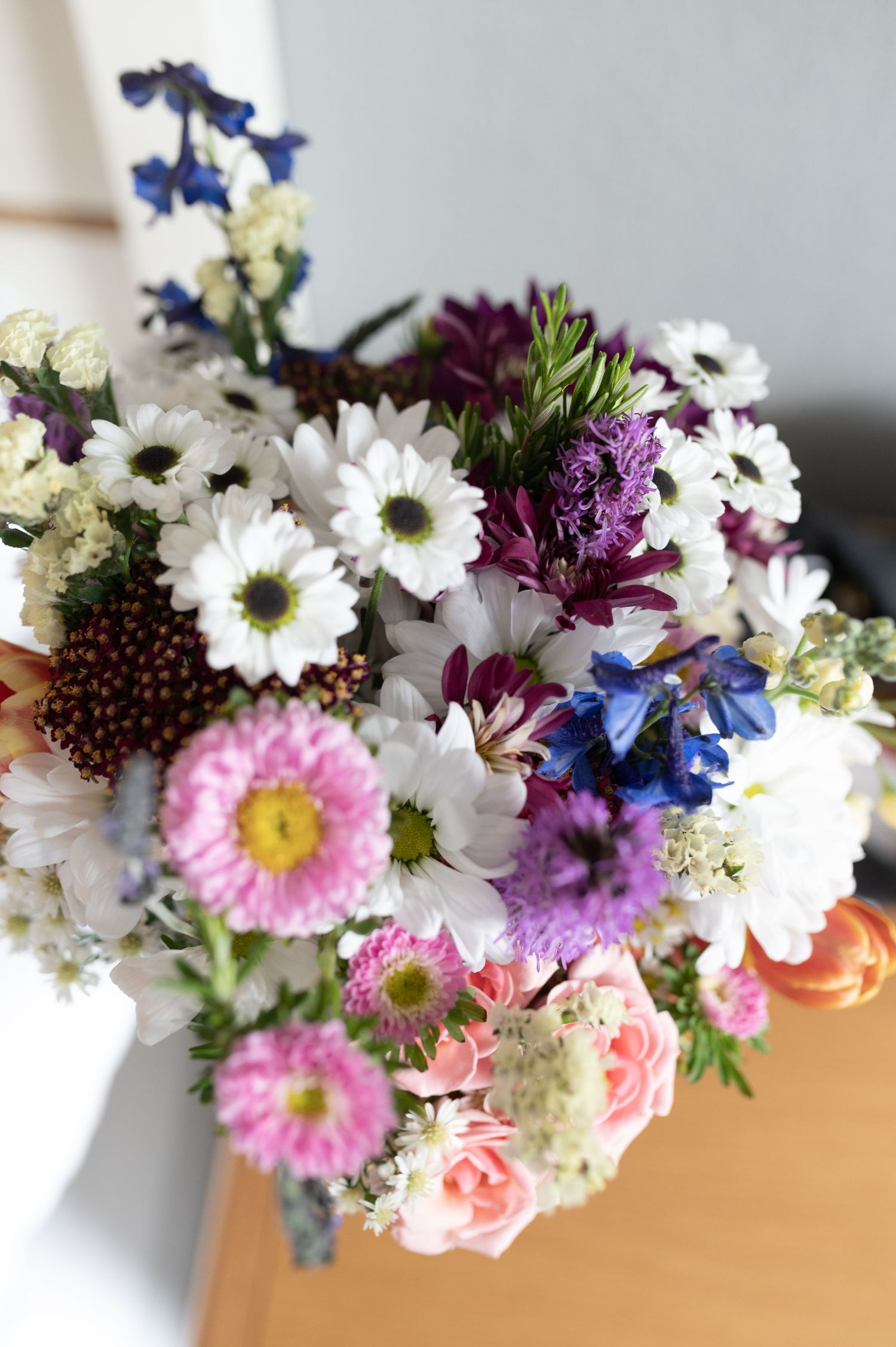 Colorful wildflower bouquet featuring daisies, pink flowers, and purple blooms on wooden surface.