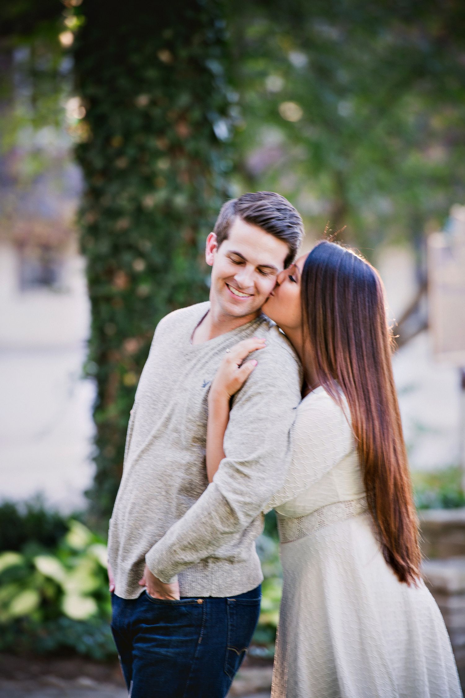 Couple laughing together during outdoor photo session with ivy covered wall.