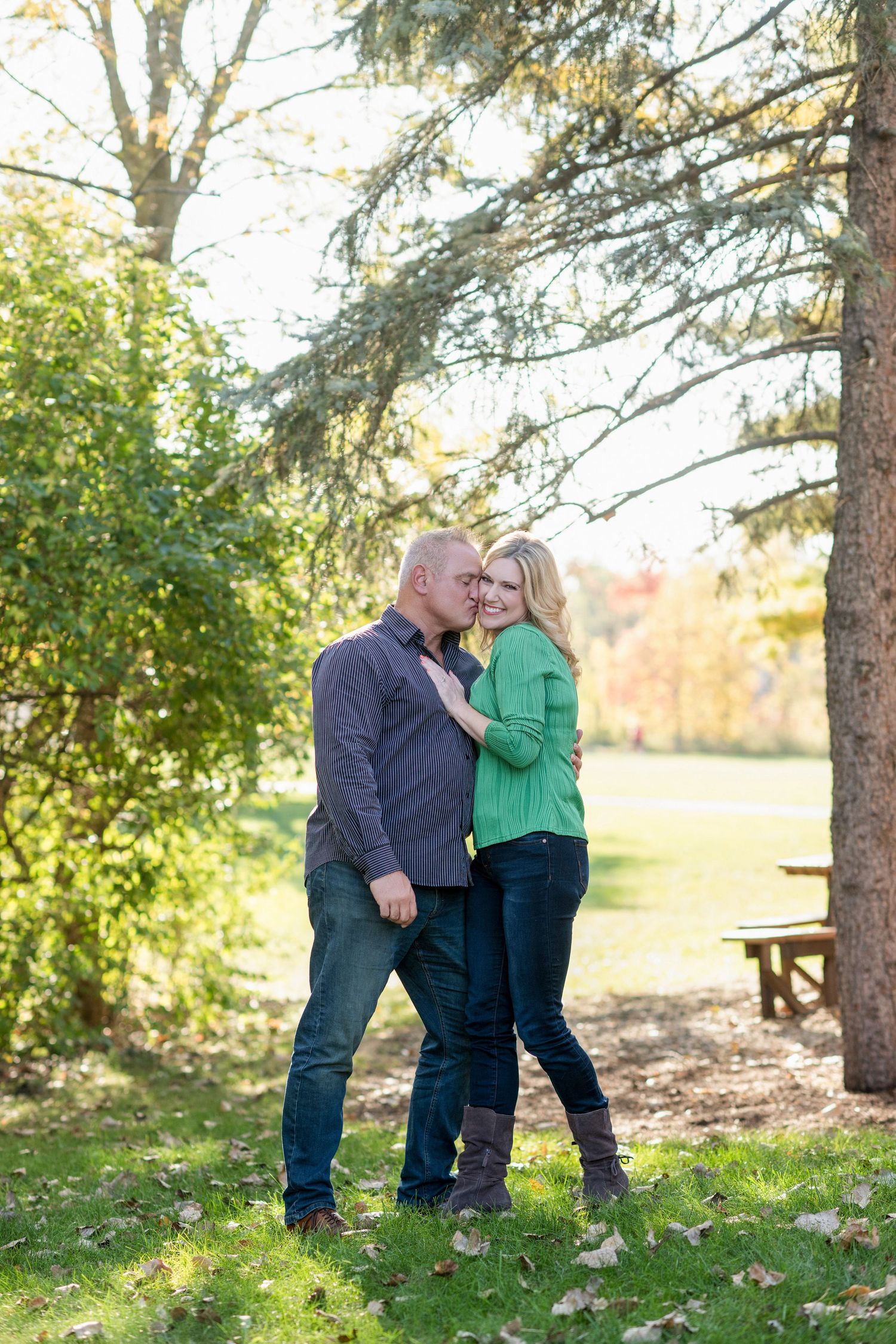 Couple sharing romantic moments in a wooded area during autumn with golden sunlight filtering through trees.
