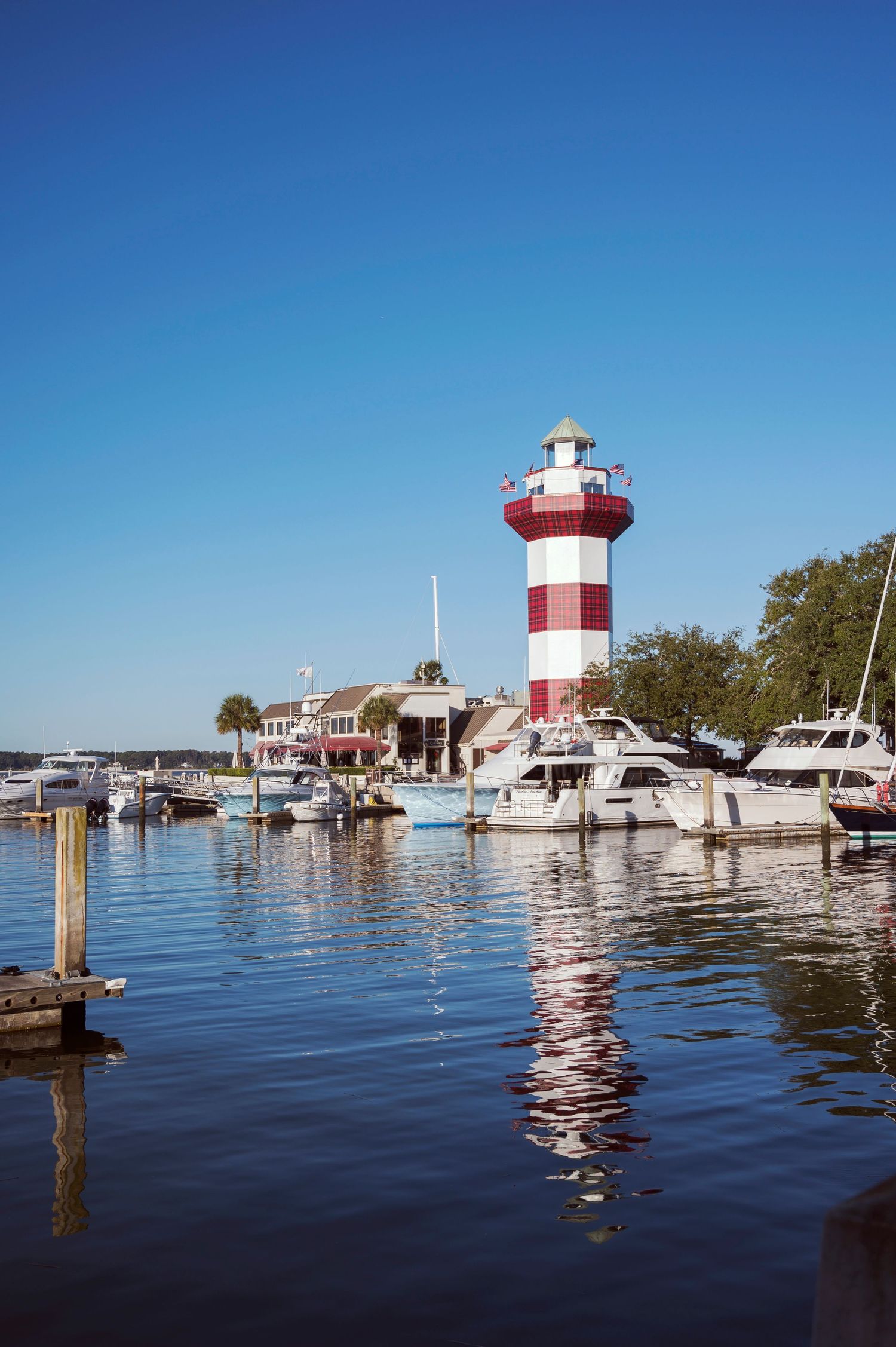 Iconic red and white Harbour Town lighthouse with boats docked at marina.