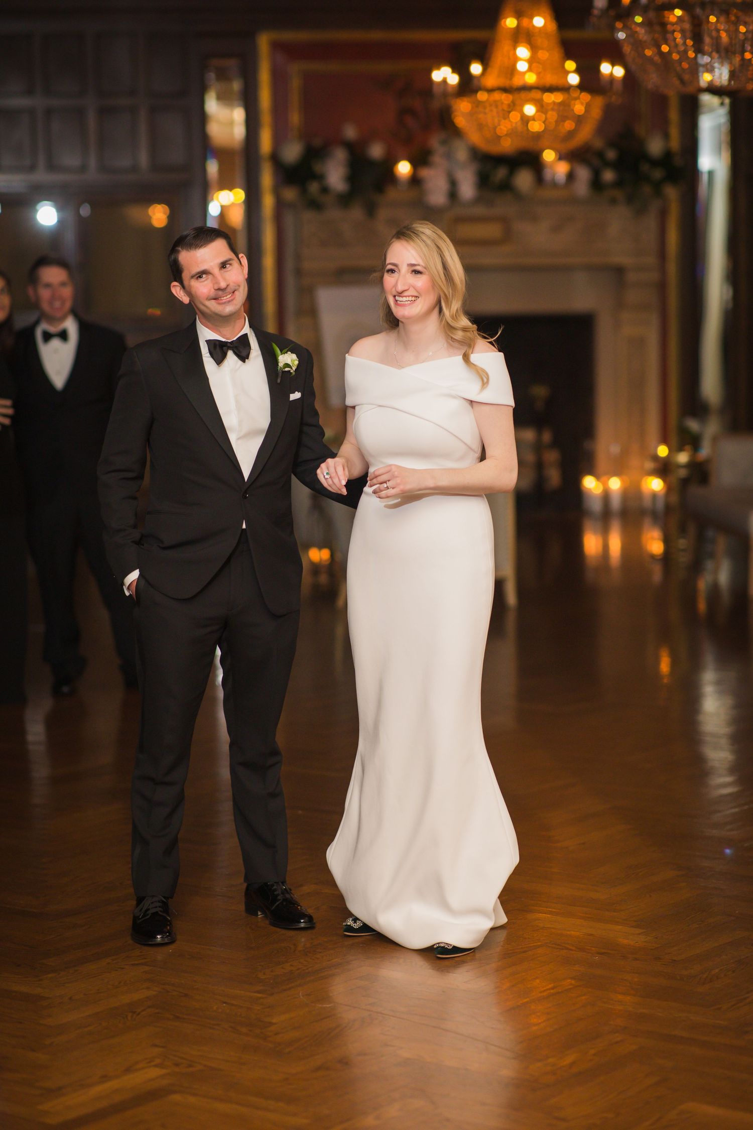 Formal couple walking through an elegant venue with chandelier lighting.