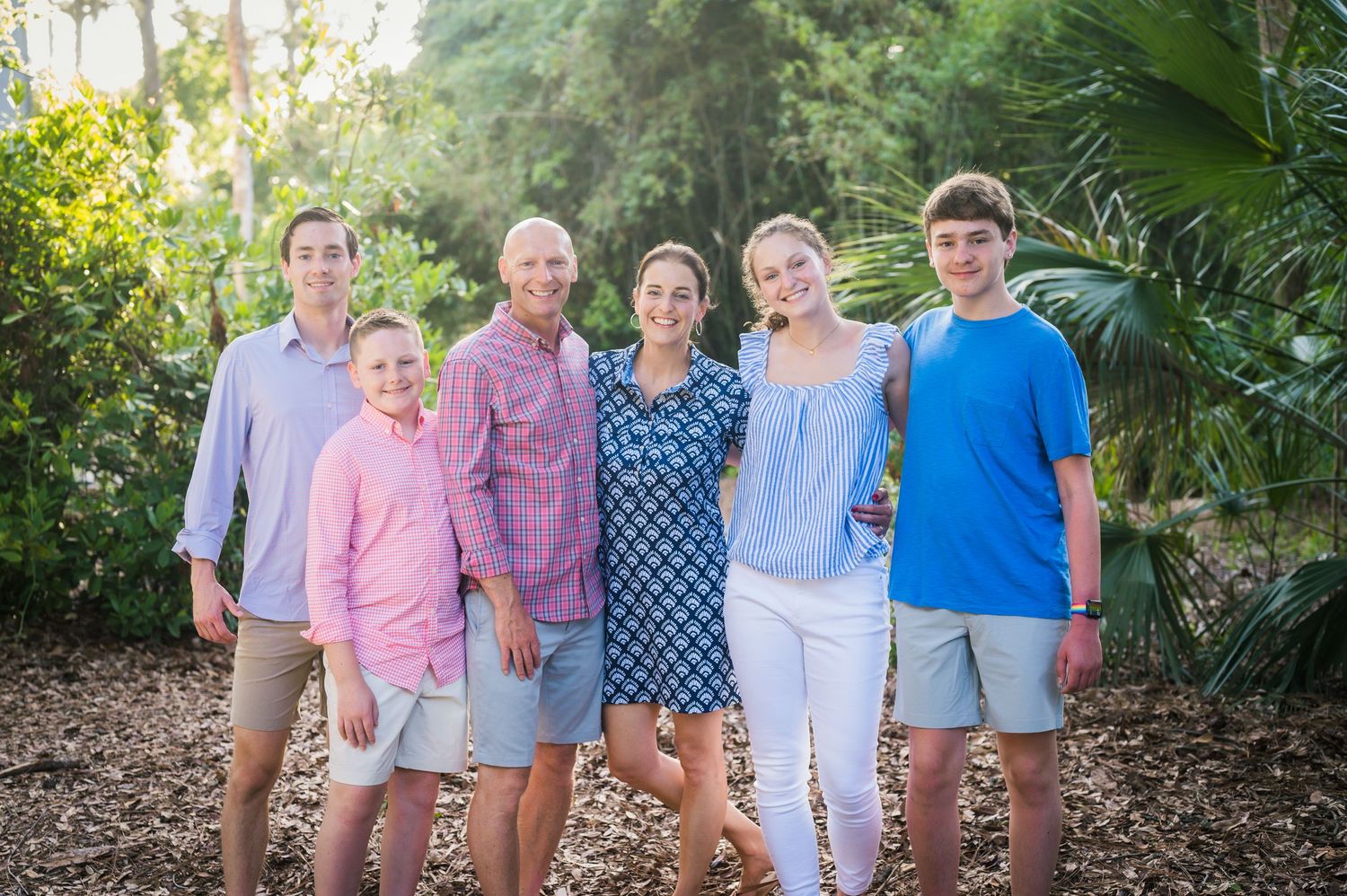 Group photo of family members coordinated in blue and pink outfits against tropical foliage.