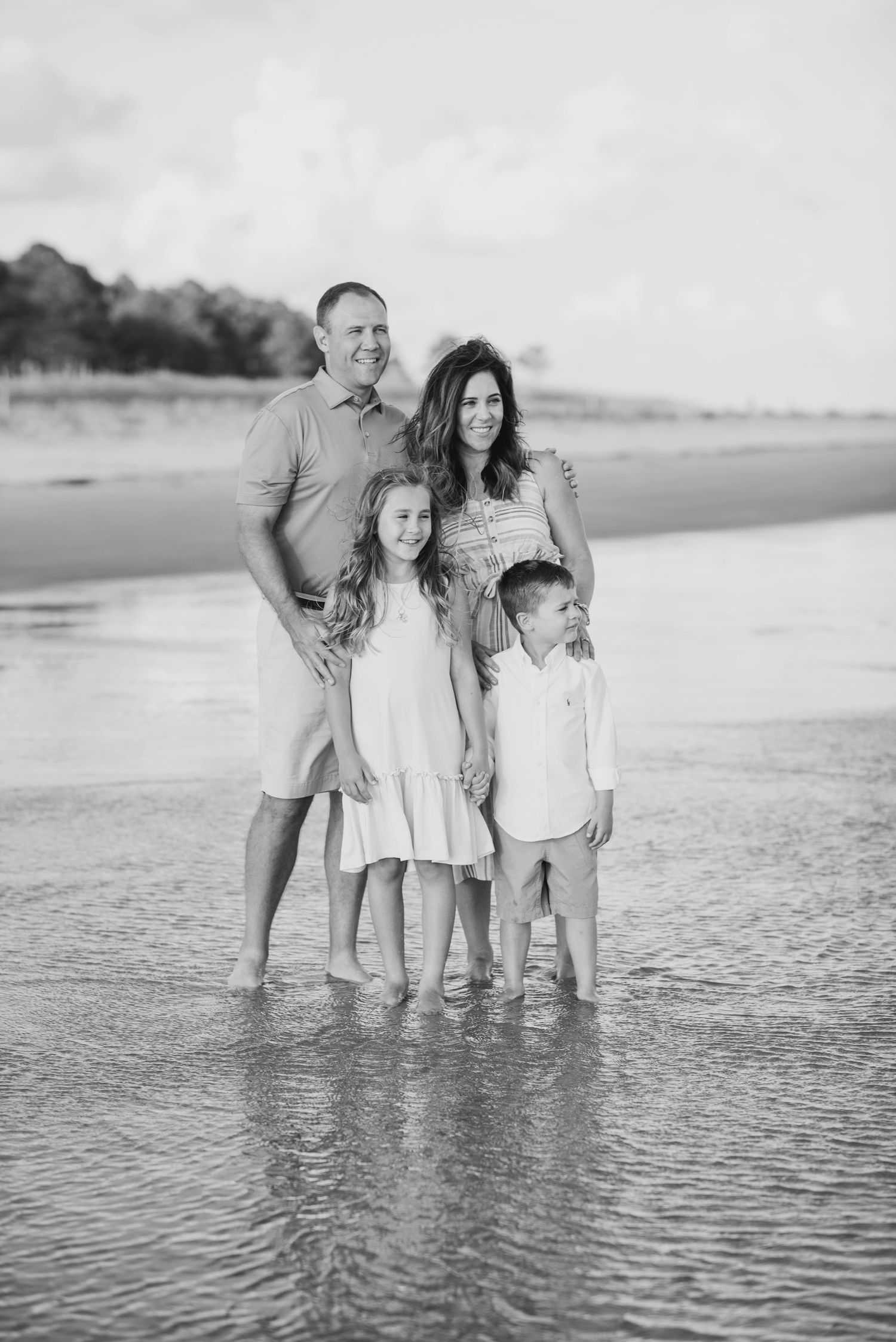 Black and white capture of family standing together in shallow ocean waves.